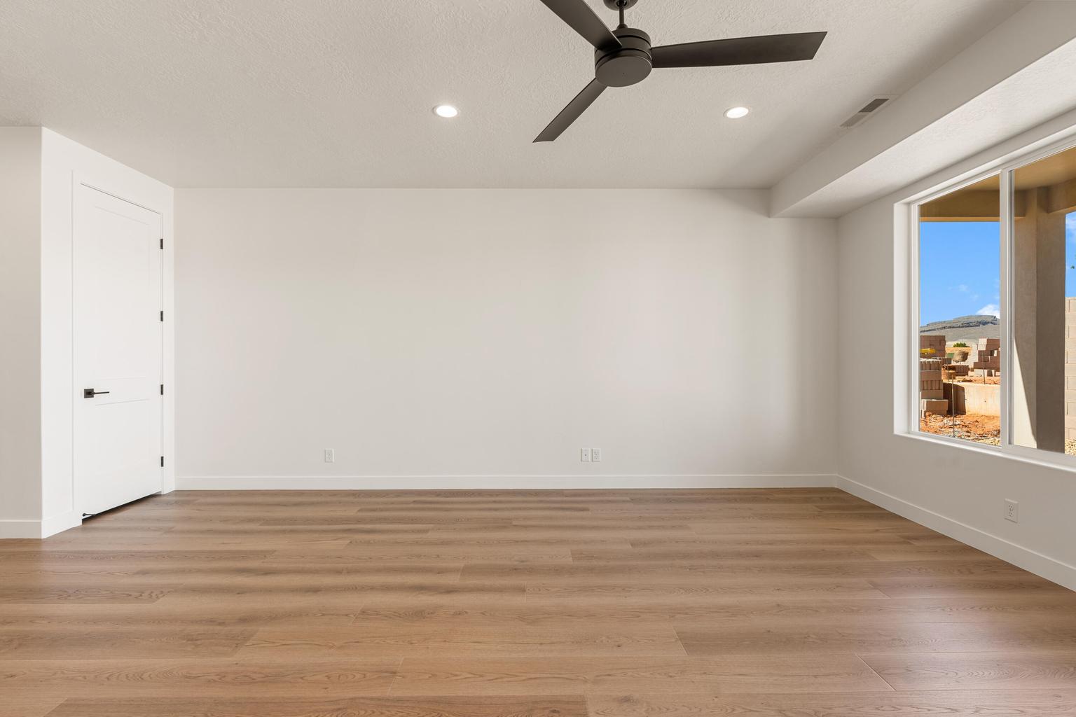 Spacious room featuring wood-finish flooring, a contemporary ceiling fan, recessed lighting, and a large window