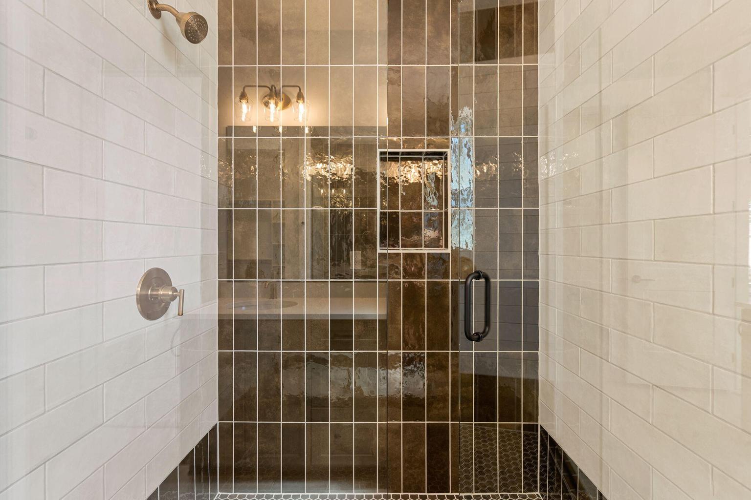 Tiled shower enclosure featuring a clear glass door, recessed shower niche, and a bronze-finish shower head and control