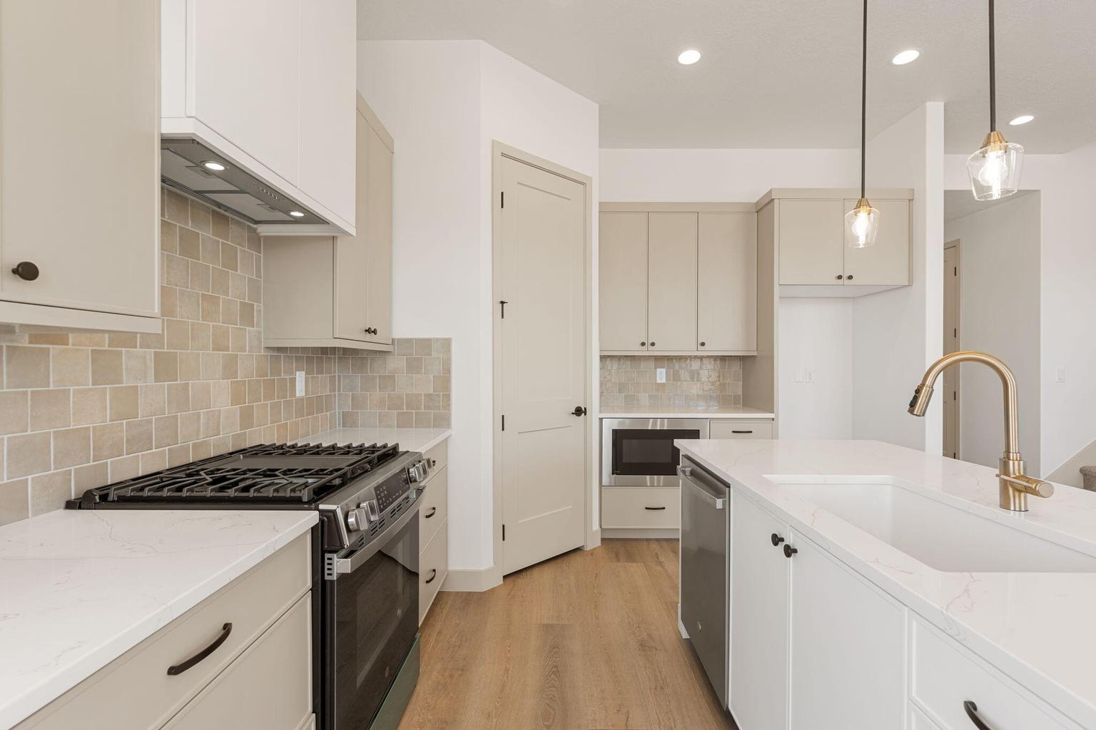 Contemporary kitchen featuring light wood-finish flooring, light grey cabinetry, white countertops, and a full-height tile backsplash