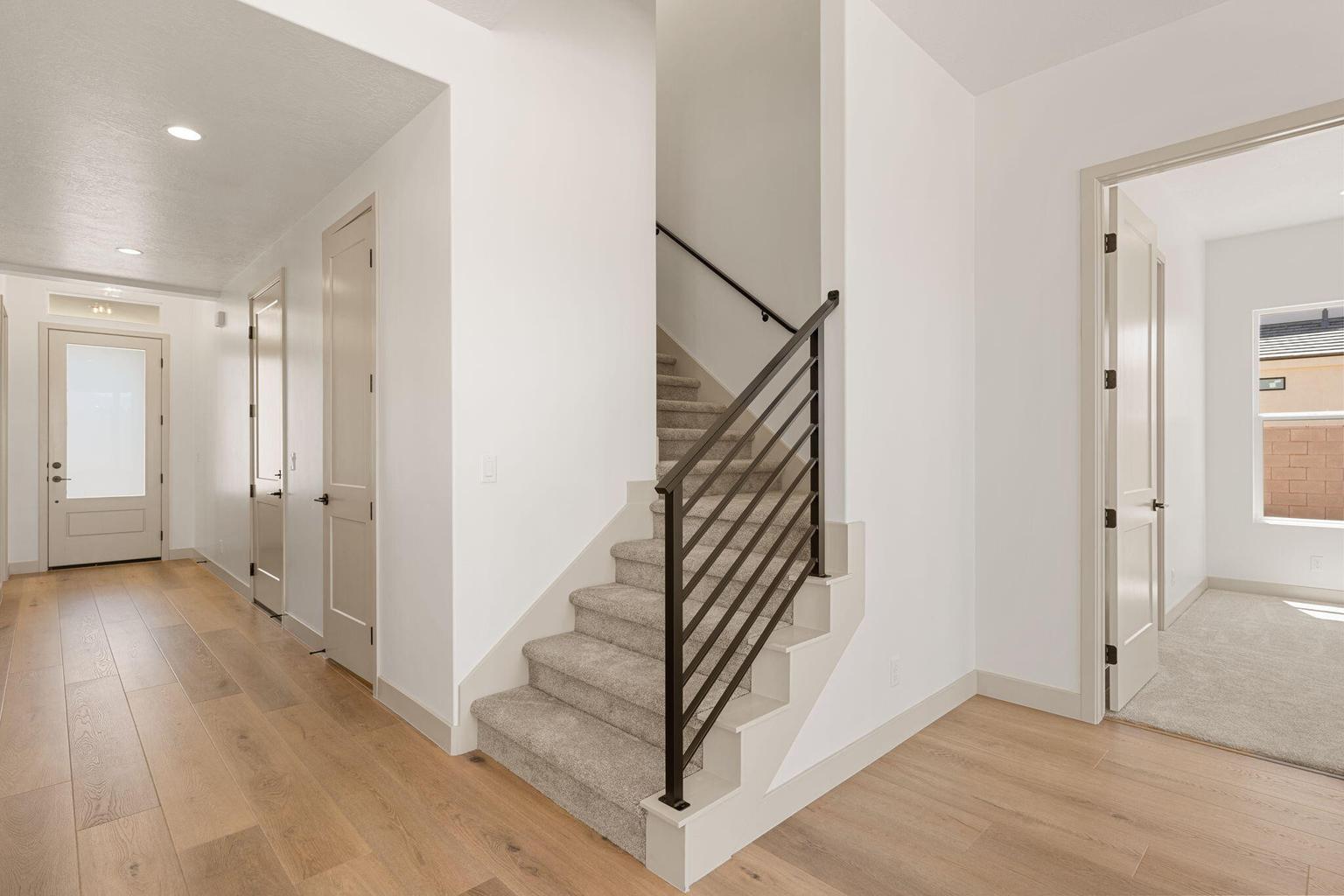Interior featuring a modern staircase with metal railings, light wood-finish flooring, recessed lighting, and a frosted glass entry door