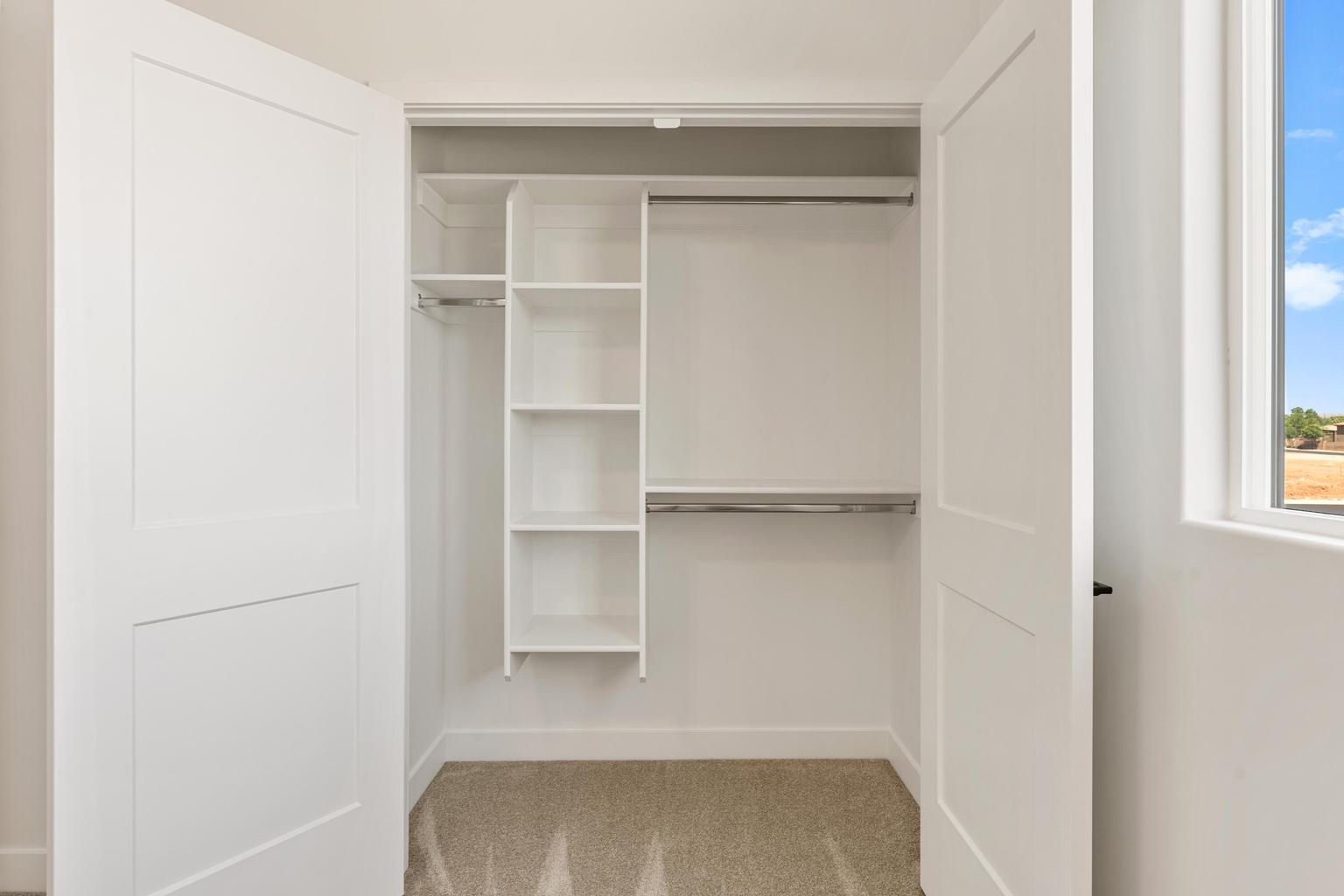 Spacious walk-in closet featuring white panel doors, built-in shelving, two clothing rods, and carpeting