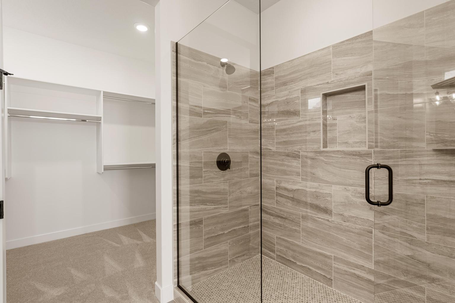 Glass-enclosed shower featuring large format tile with a built-in niche and contrasting dark bronze hardware