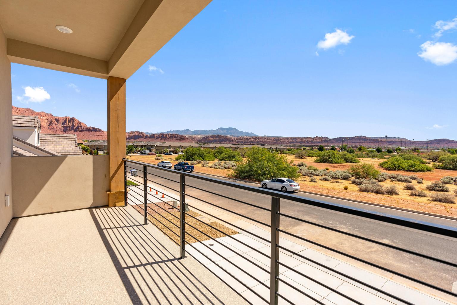 Covered balcony with textured flooring, featuring a contemporary metal railing, recessed lighting, and expansive desert and mountain scenery