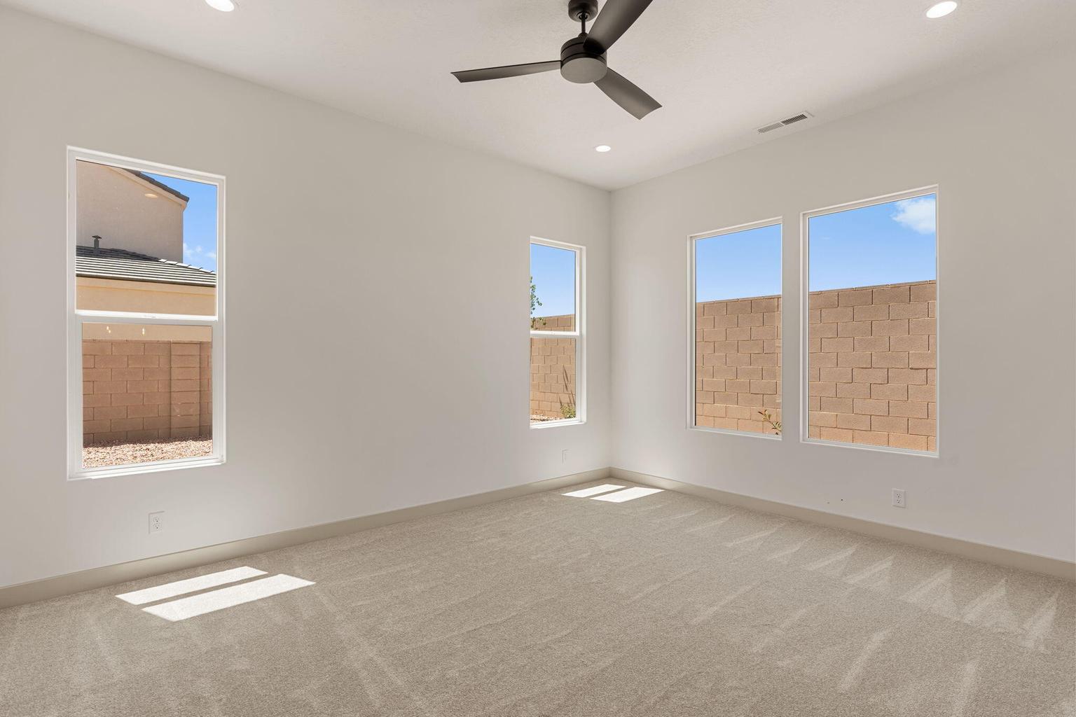 Spacious room featuring neutral carpeting, recessed lighting, a ceiling fan with integrated light, and multiple windows