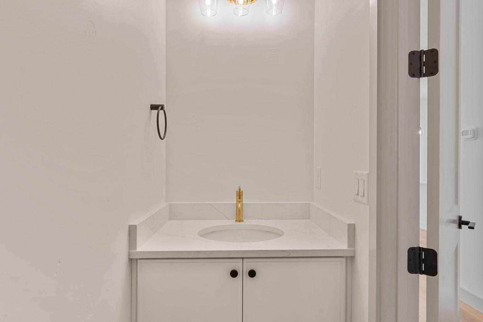 Bathroom vanity featuring a gold-finish faucet, undermount sink, quartz countertop, and white cabinetry with matte black hardware