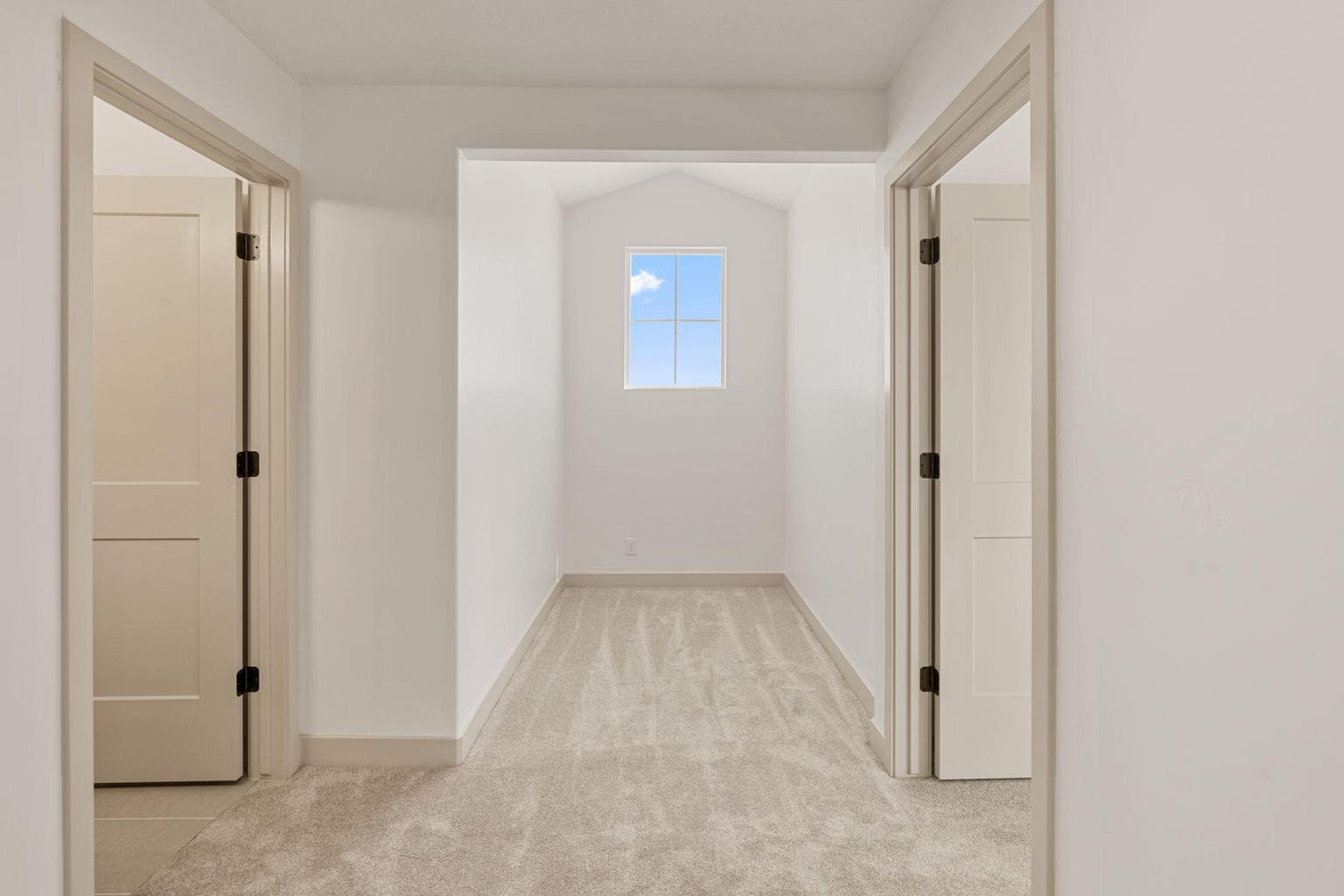 Bright hallway featuring light-toned carpet flooring, white walls, and a window providing natural light