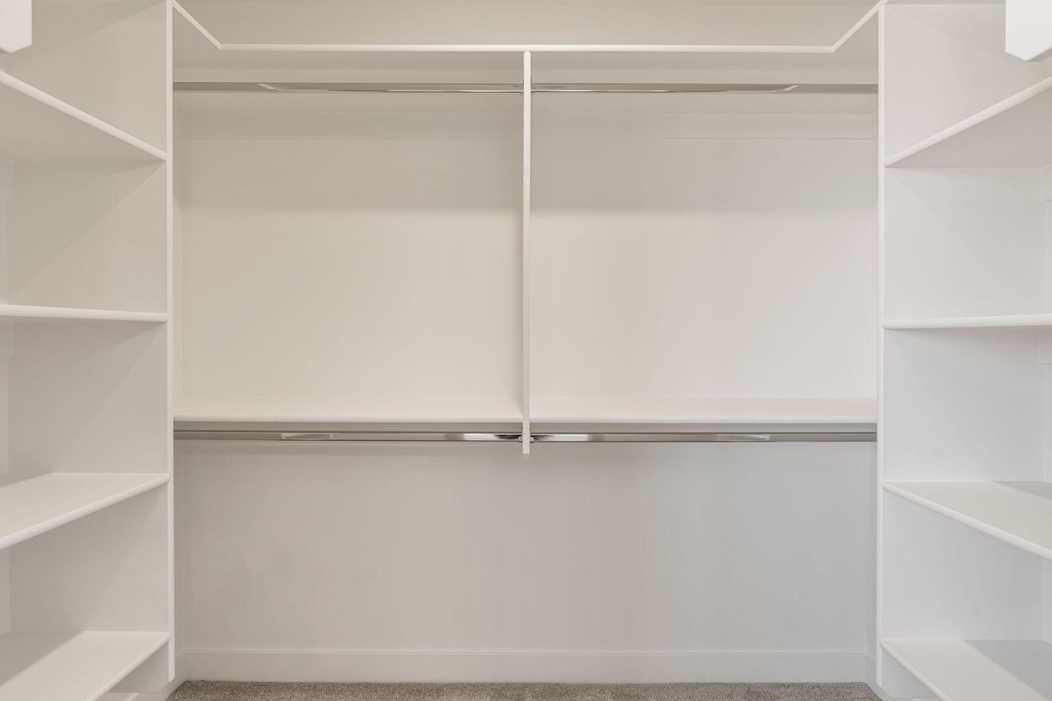 Built-in closet system featuring white shelving, multiple hanging rods, and light-toned carpeting
