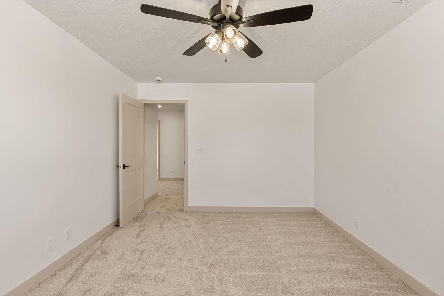 Neutral color palette featuring light beige carpeting, white walls, and a contemporary ceiling fan with four light fixtures