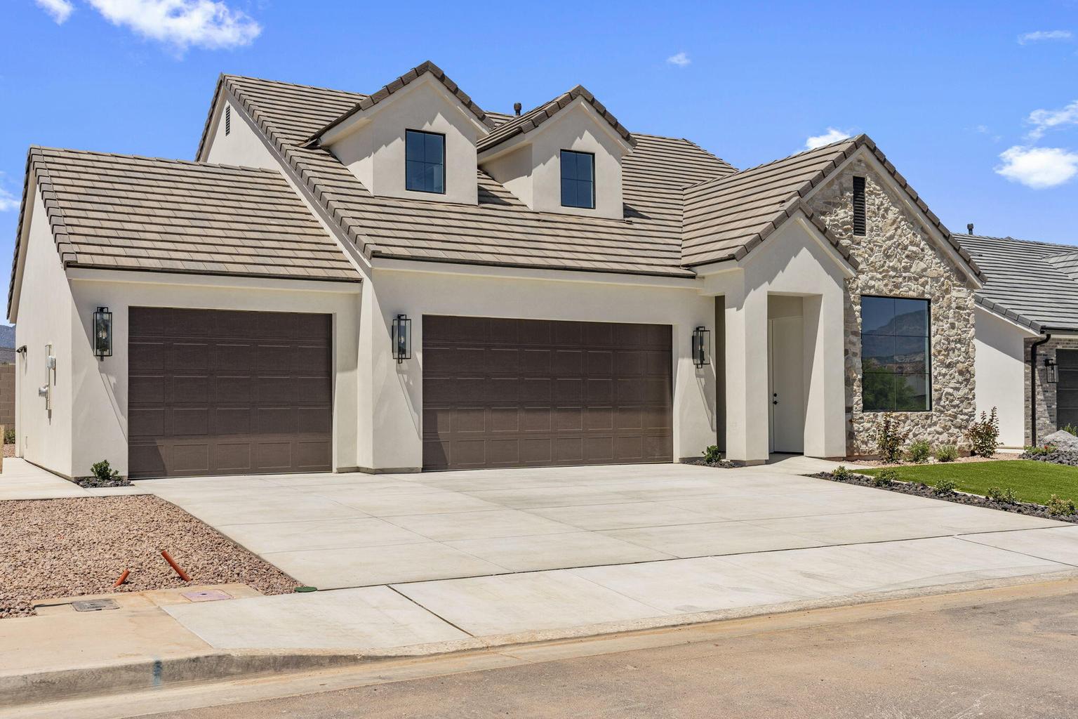 Modern stucco exterior featuring a stone accent wall, tiled roof, two brown garage doors, and a concrete driveway