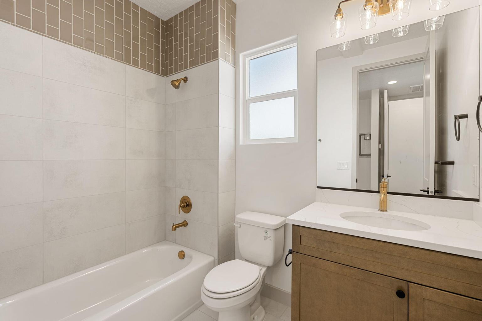 Bathroom featuring a white subway tile surround with a decorative subway tile accent, a white tub, and brass fixtures
