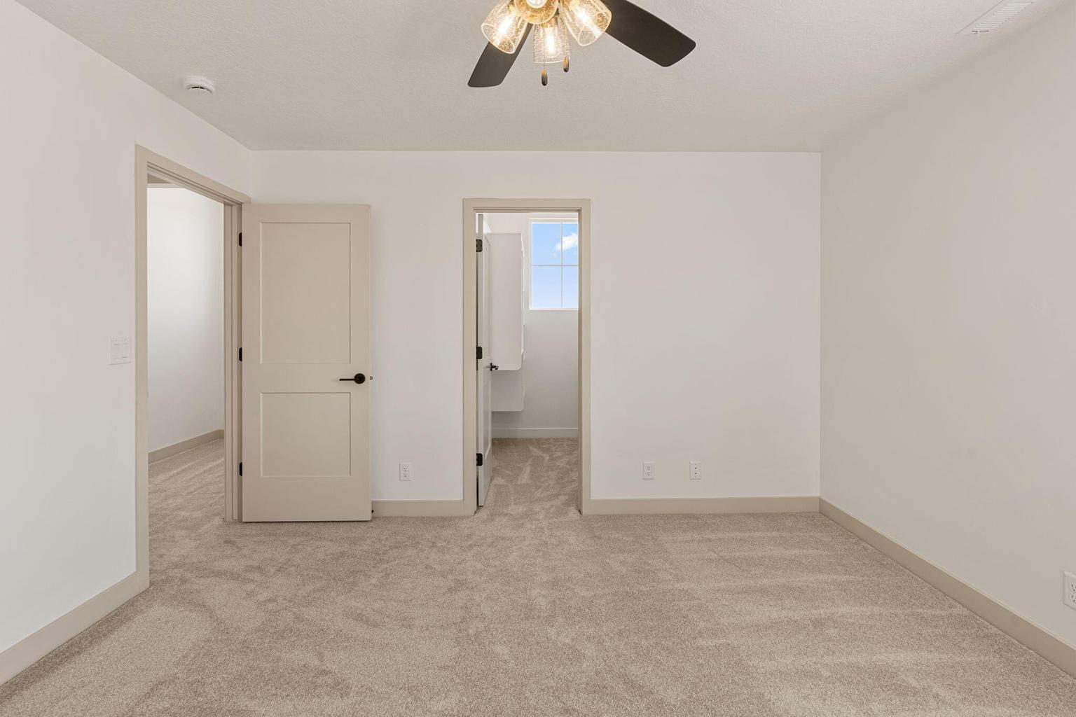 Carpeted interior space with two interior doorways, a ceiling fan with light fixture, and neutral wall tones