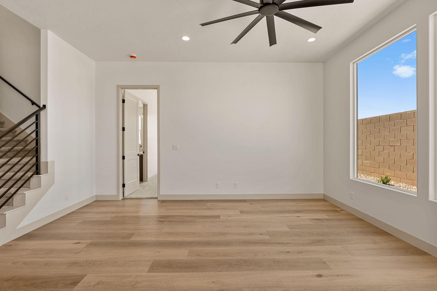 Open-concept living space with light wood-finish flooring, a contemporary ceiling fan, recessed lighting, and a large window