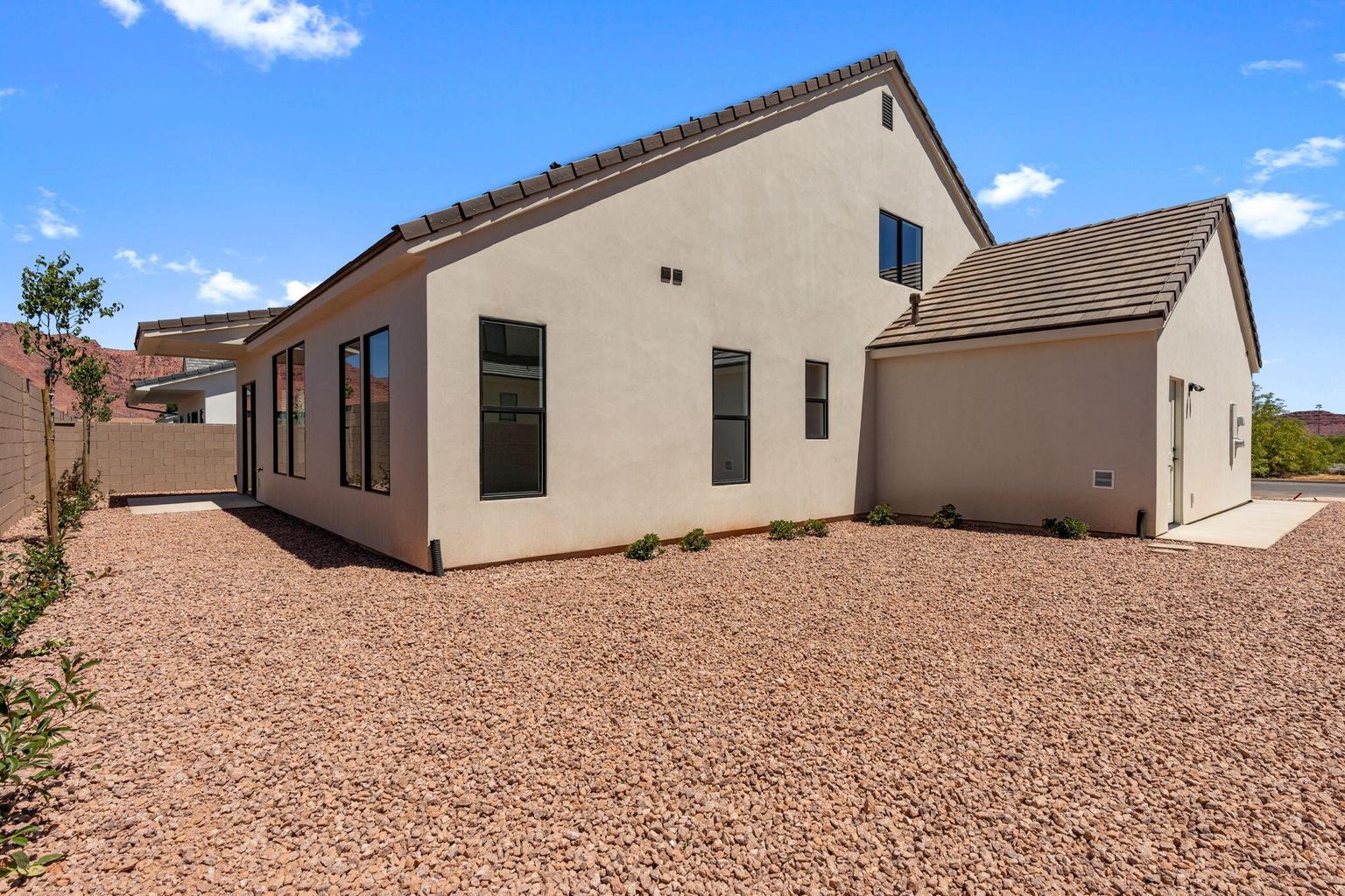 Contemporary stucco exterior with a tiled roof, multiple dark-framed windows, and an expansive gravel yard
