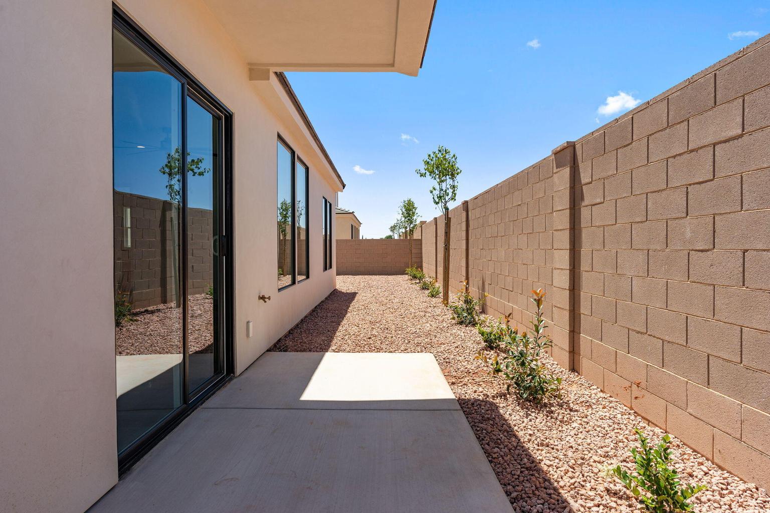 Exterior patio with a concrete slab, sliding glass door entry, multiple fixed pane windows, gravel landscaping, and a block wall perimeter