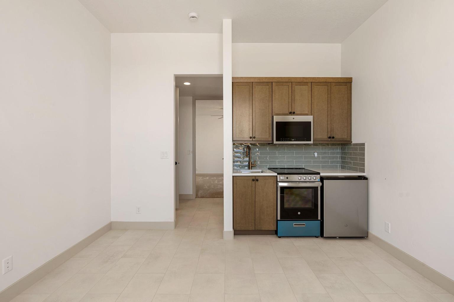 Compact kitchen area featuring wood-finish cabinetry, stainless steel appliances including a microwave and range, and a light blue subway tile backsplash