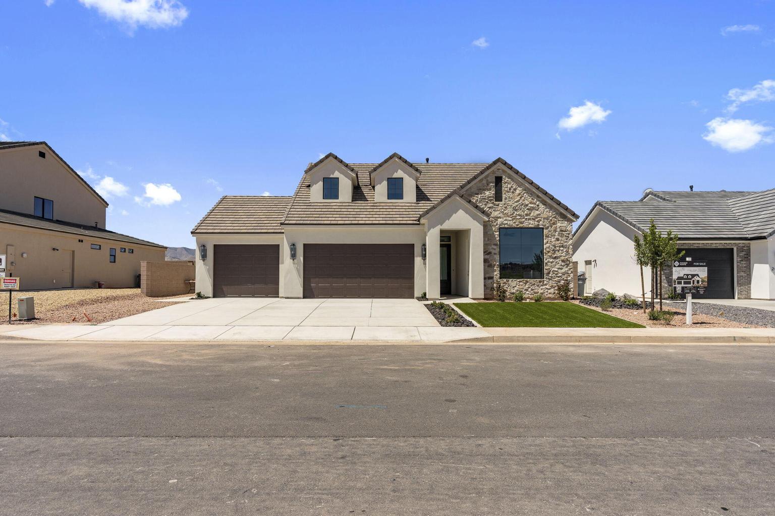 Stone facade home featuring a two-car garage, manicured lawn, and a wide driveway