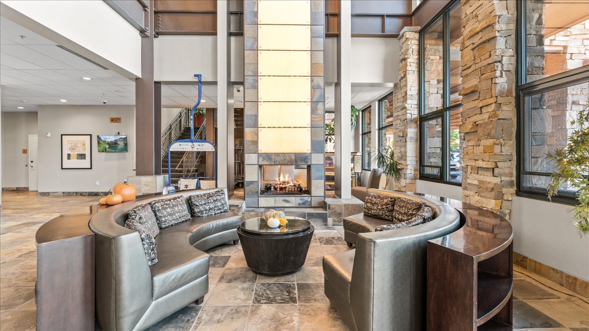 Lobby area featuring a stone-clad fireplace, large windows, high ceilings, tile flooring, and a unique ski lift chair display