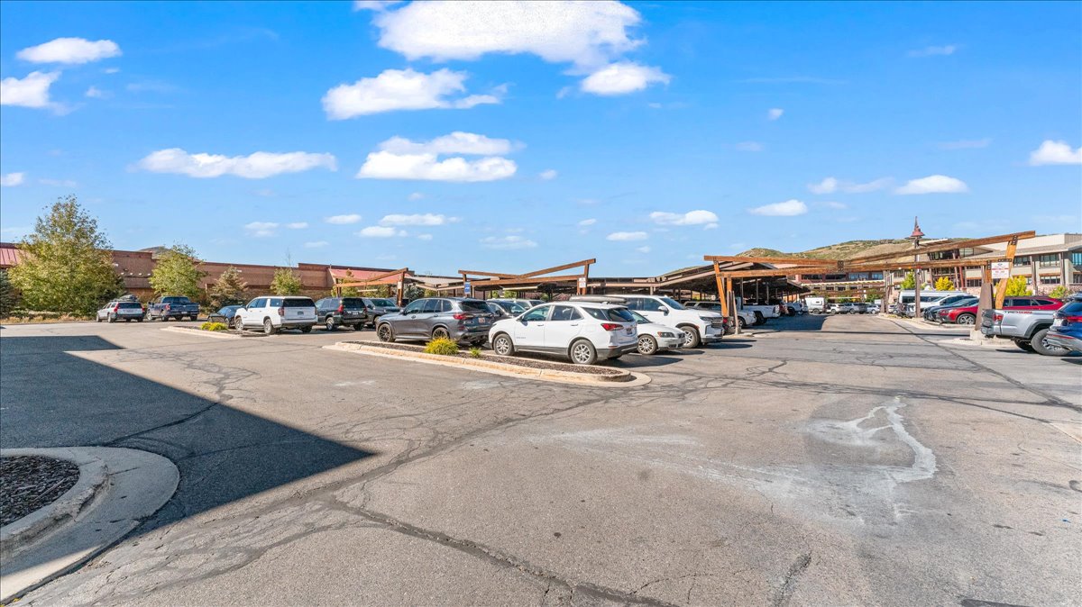 Paved parking lot with designated spaces, featuring covered parking structures with slatted roofs