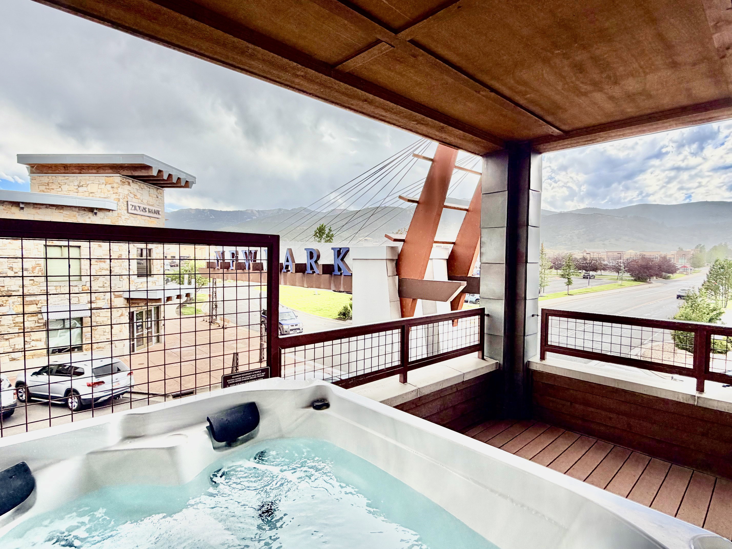 Outdoor balcony featuring an integrated hot tub, composite wood-finish decking, and metal railing