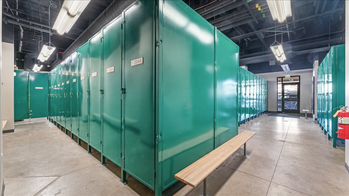 Spacious locker room featuring rows of emerald green lockers, exposed ceiling infrastructure, concrete flooring, and linear fluorescent lighting