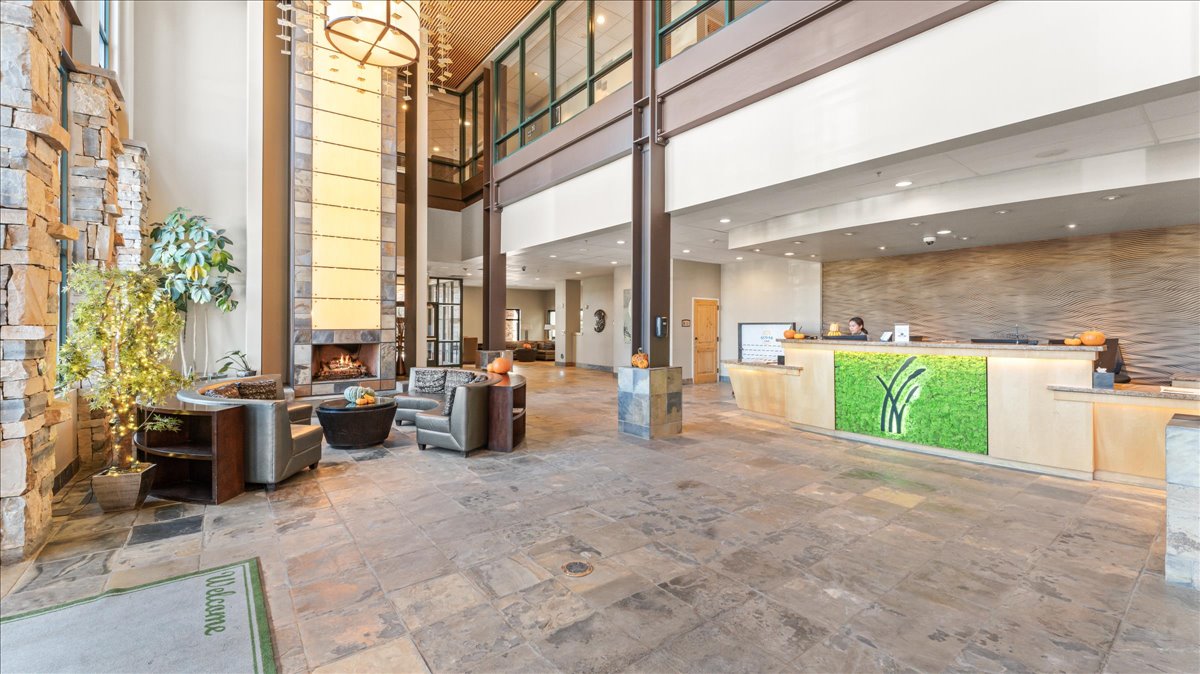 Spacious lobby featuring a stone accent wall, multi-level ceilings, a central fireplace, an illuminated reception desk, and stone tile flooring