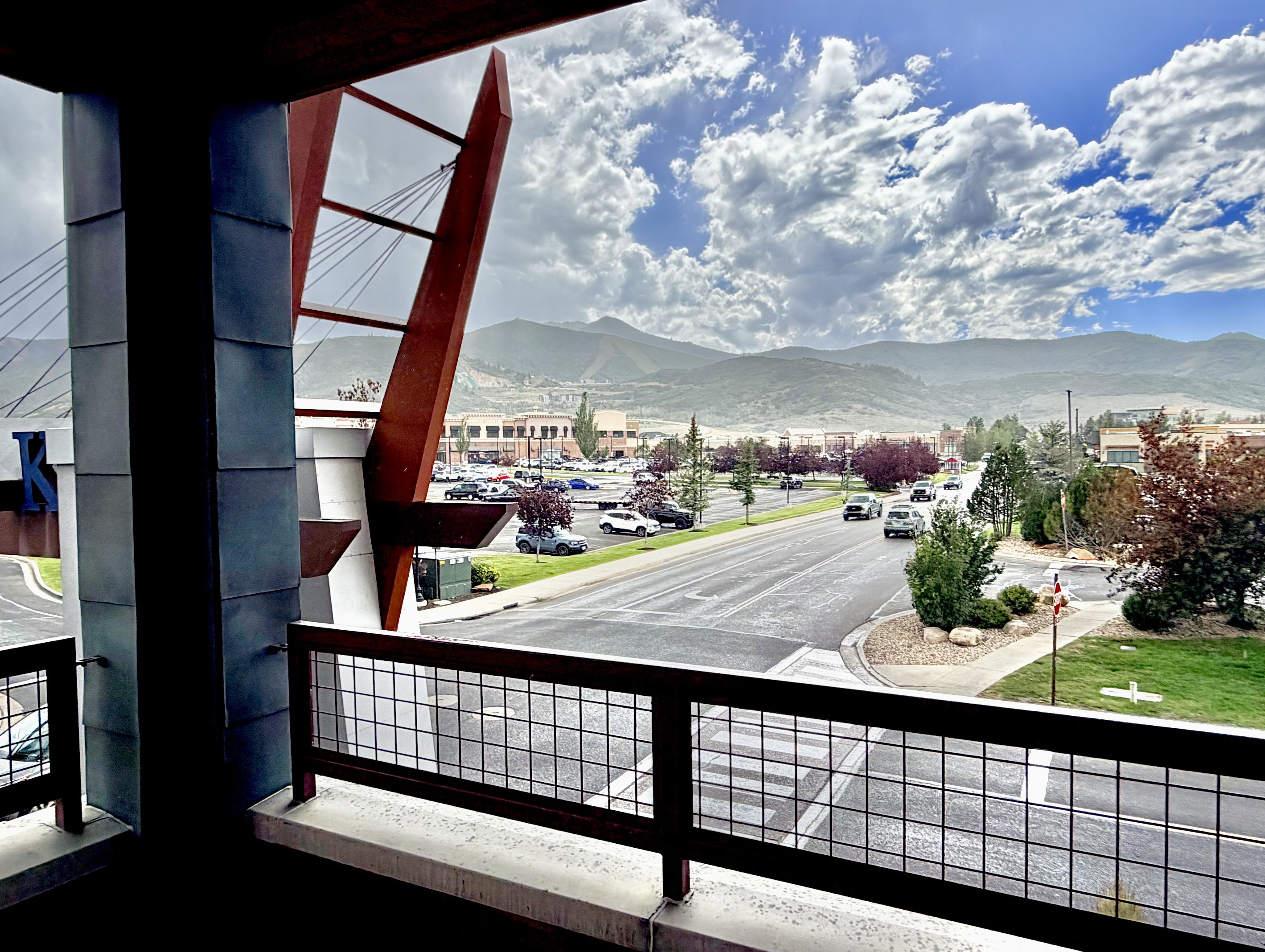 Balcony featuring a metal grid railing overlooking a street with mountain scenery