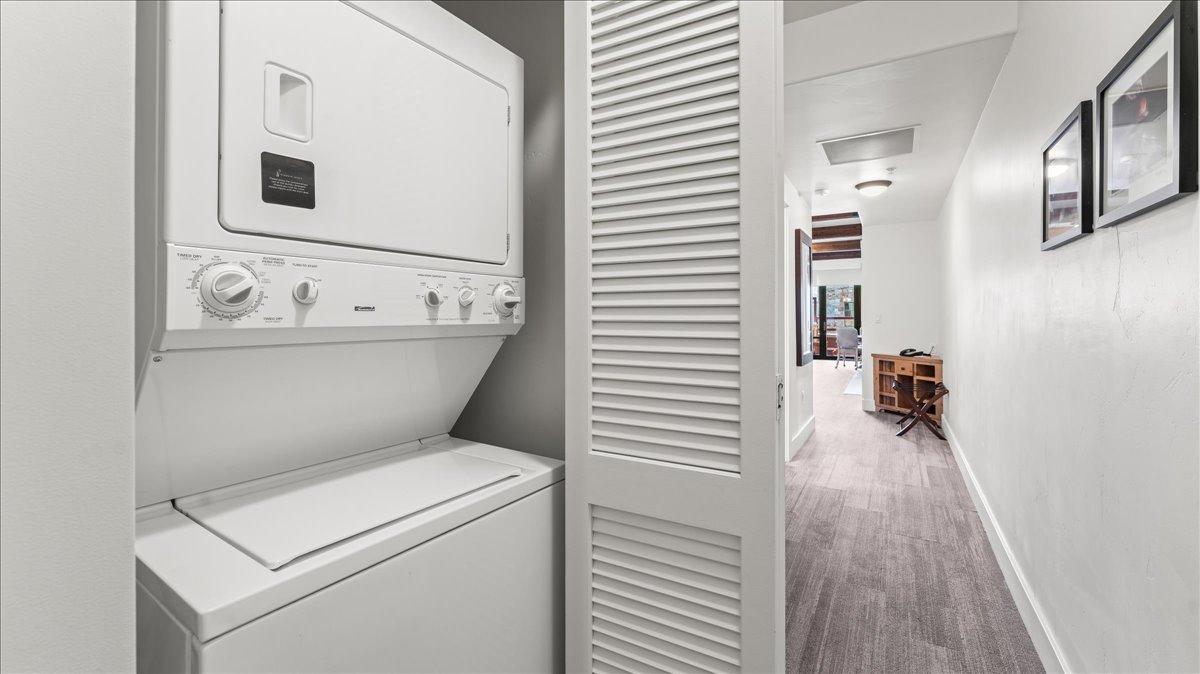 Dedicated laundry closet featuring a stacked washer and dryer, louvered bi-fold door, and wood-finish flooring extending into the hallway