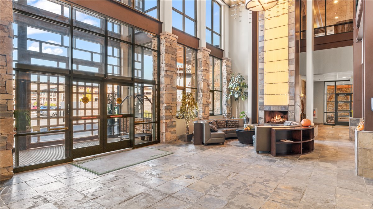 Spacious lobby featuring stone flooring, a two-story stone fireplace, full-height window walls, and wood-paneled accents