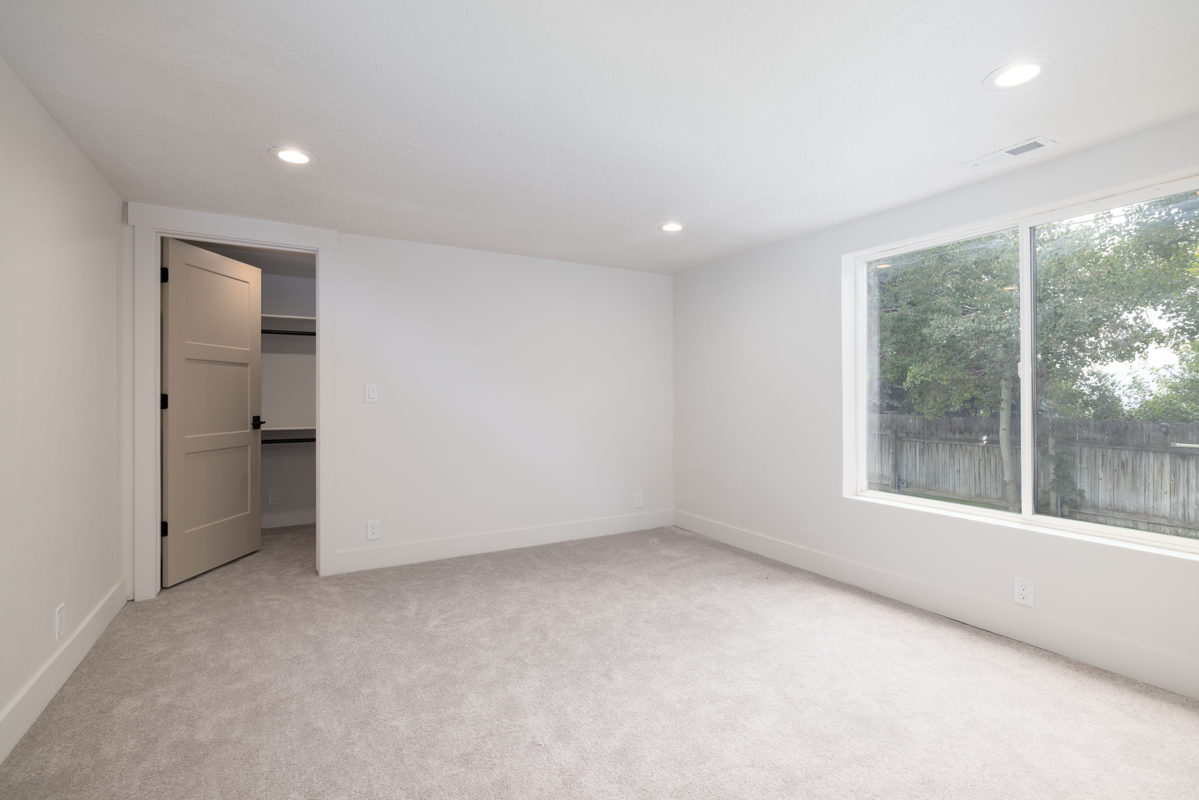 Carpeted room with recessed lighting and a large window featuring a tree-lined exterior