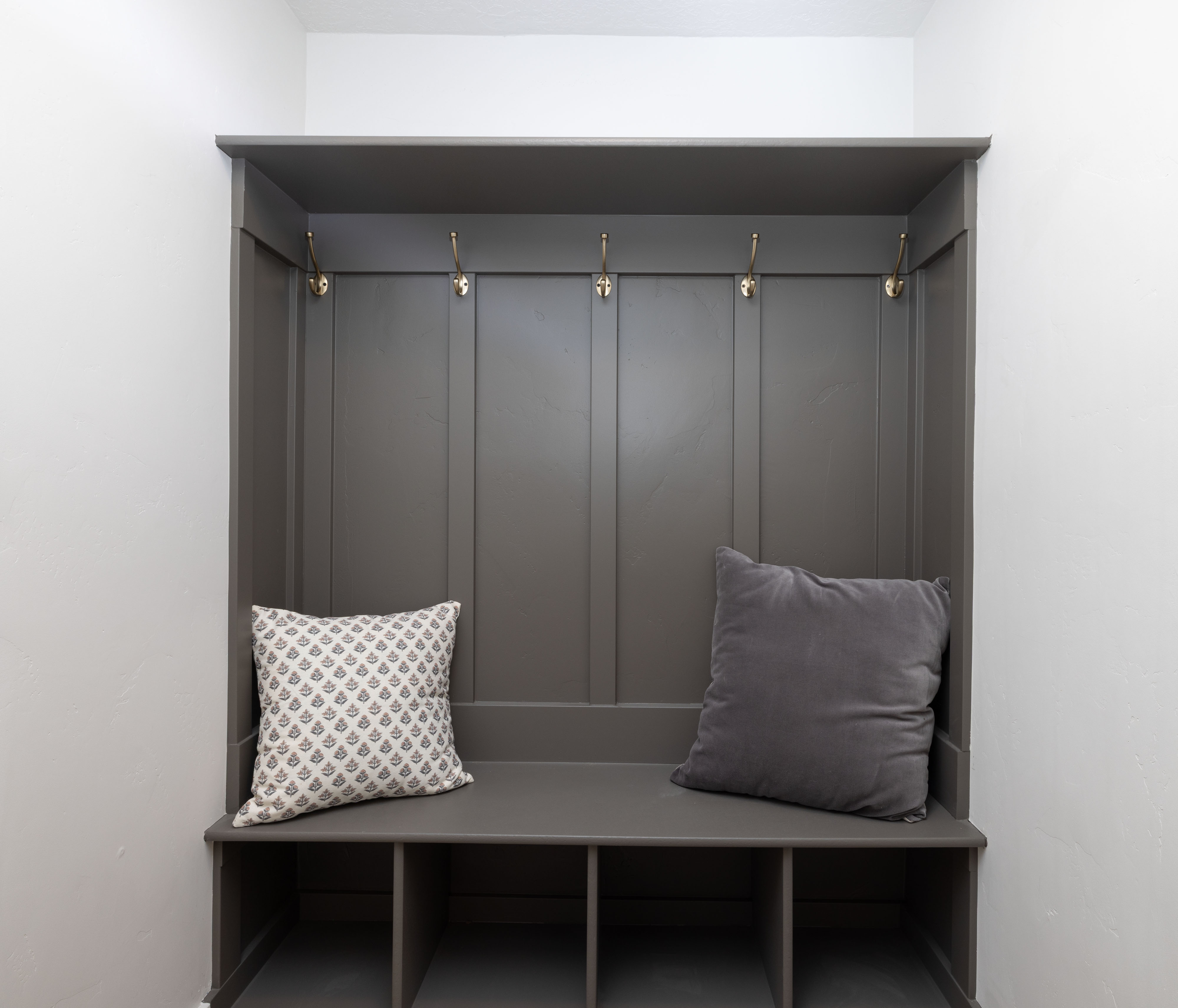 Built-in mudroom bench featuring paneled backing, four brass-finish hooks, and four lower cubbies