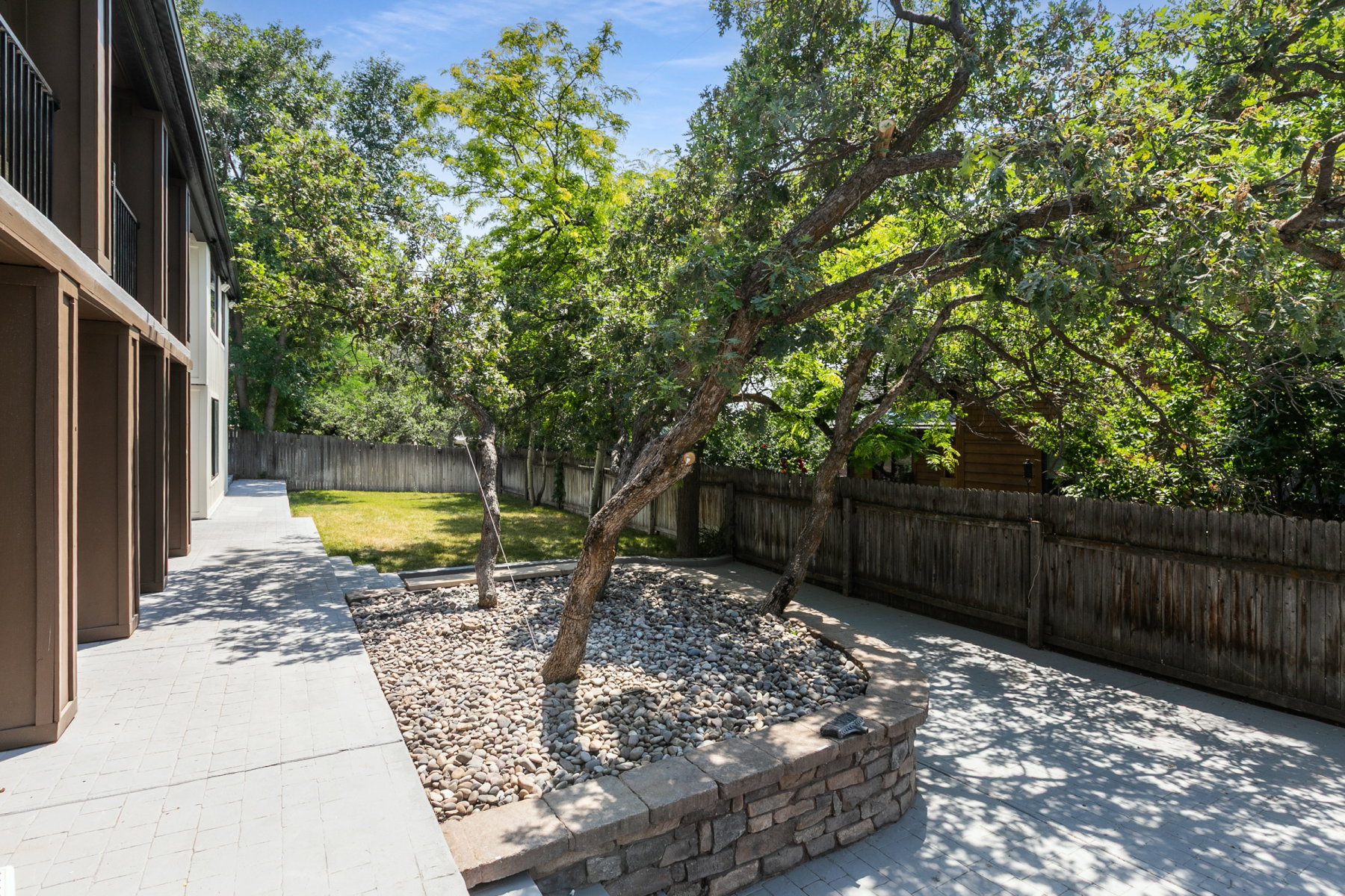 Paved patio area featuring a stone-clad retaining wall and two mature trees