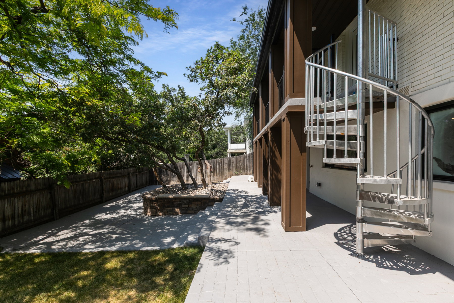 Outdoor patio featuring a spiral staircase, established trees, and a stone-built planter