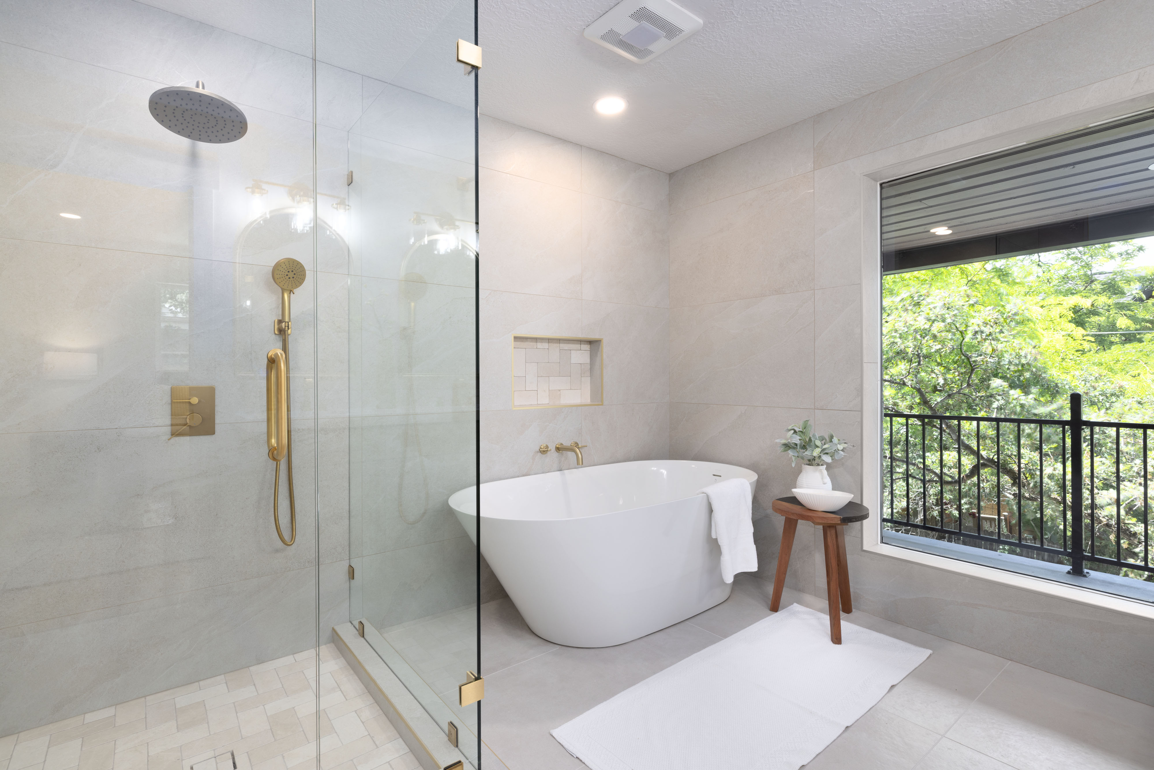 Contemporary bathroom featuring a freestanding soaking tub, a frameless glass shower enclosure with gold-tone fixtures, and a recessed tiled niche