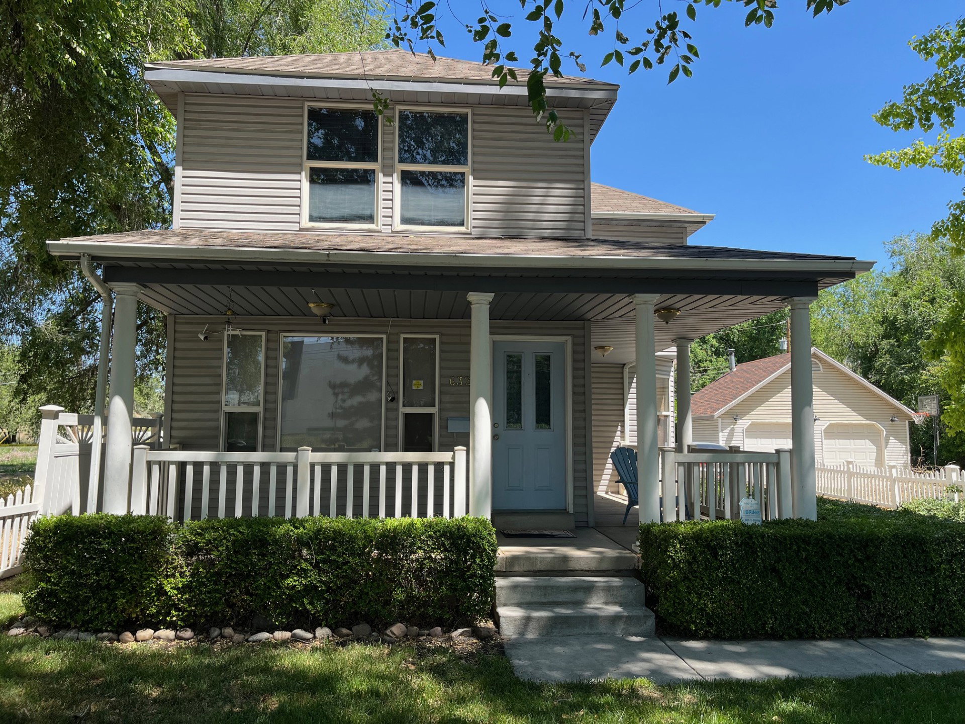 Two-story residence featuring light gray siding, a covered front porch with white columns and railings, and a detached two-car garage