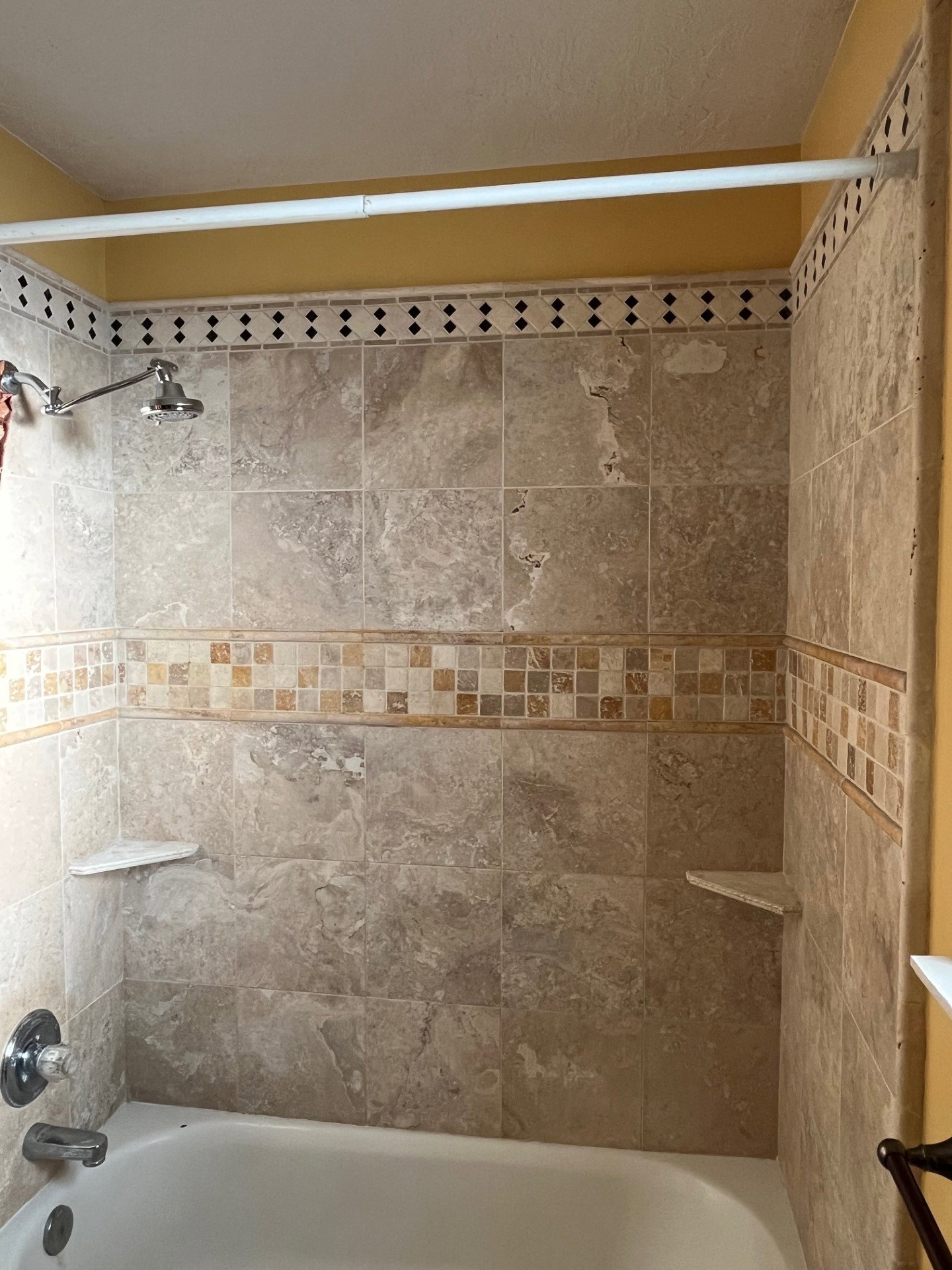 Bathtub with tiled surround featuring mosaic accents, an adjustable shower head, and built-in corner shelving