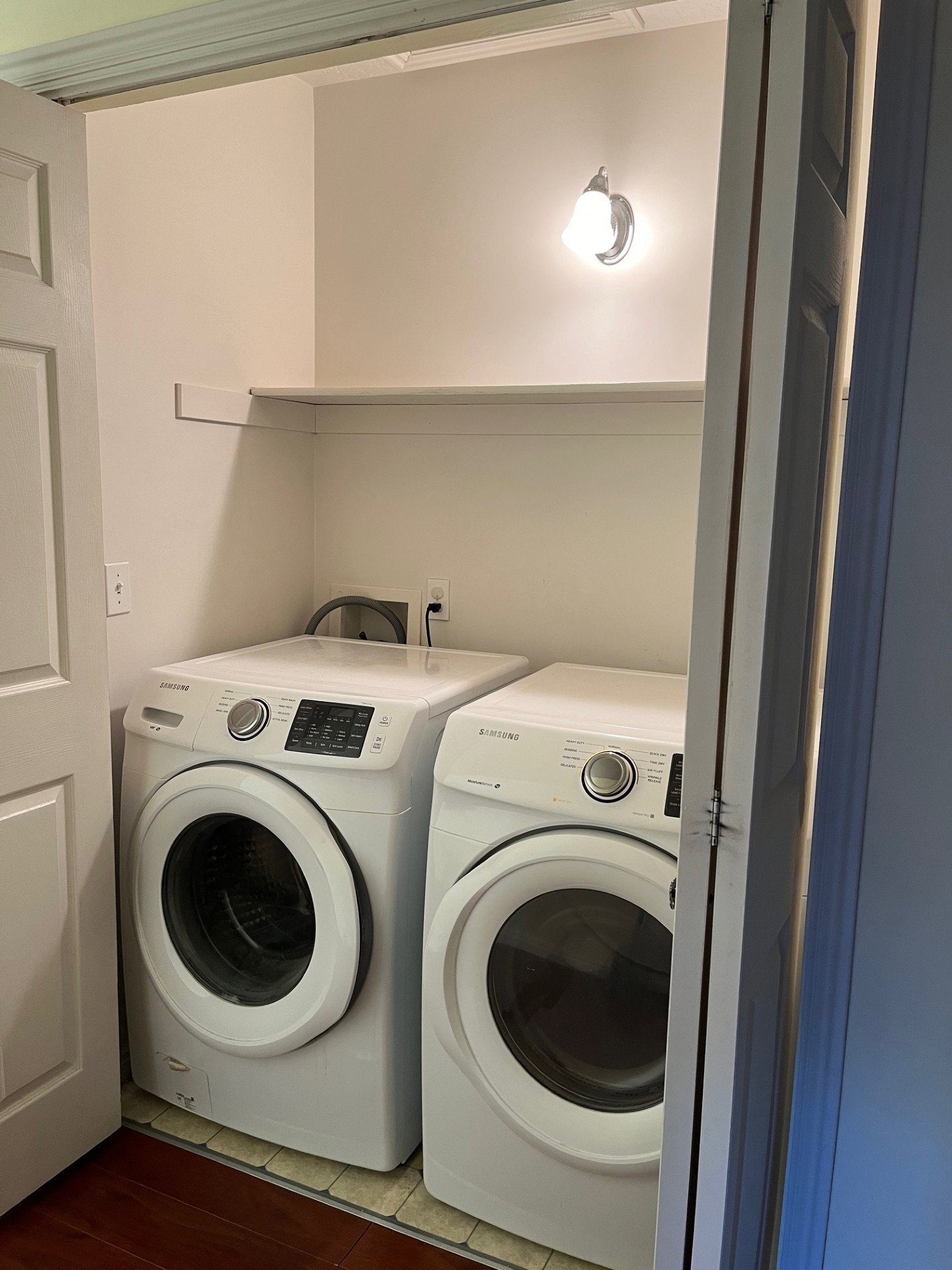 Dedicated laundry area featuring a wall-mounted sconce, built-in shelving, wood-finish flooring, and white bifold doors