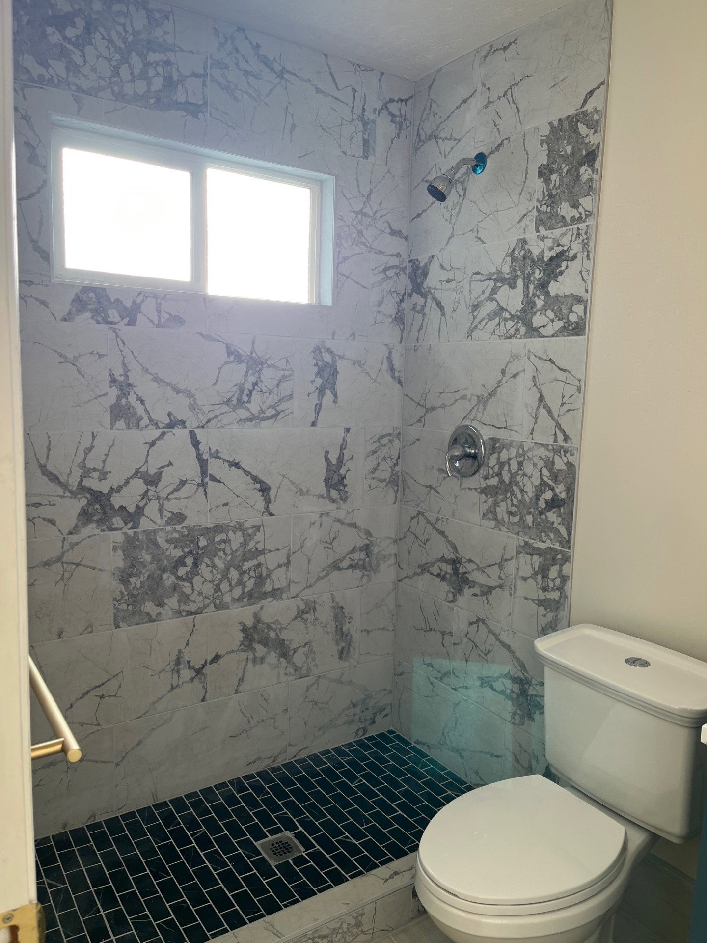 Walk-in shower with large format marble-look tile walls, black subway tile floor, and a chrome shower head