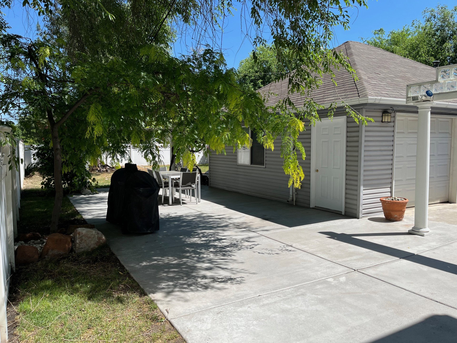 Expansive concrete patio area featuring a mature shade tree, a separate access door on the adjacent structure, and a gray siding exterior