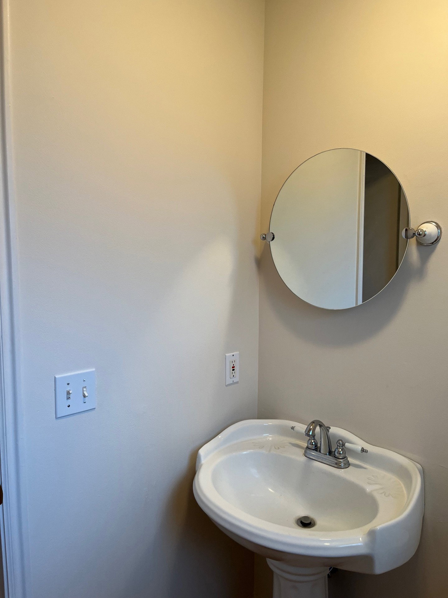 Pedestal sink with chrome-finish faucet and a wall-mounted circular mirror