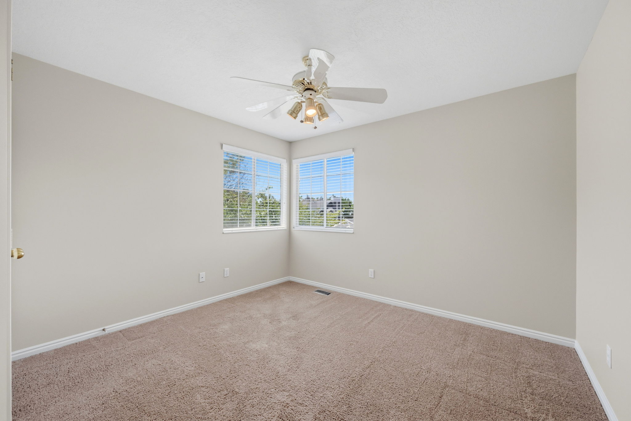 Carpeted room featuring two windows with blinds, a ceiling fan with integrated lighting, and neutral wall tones