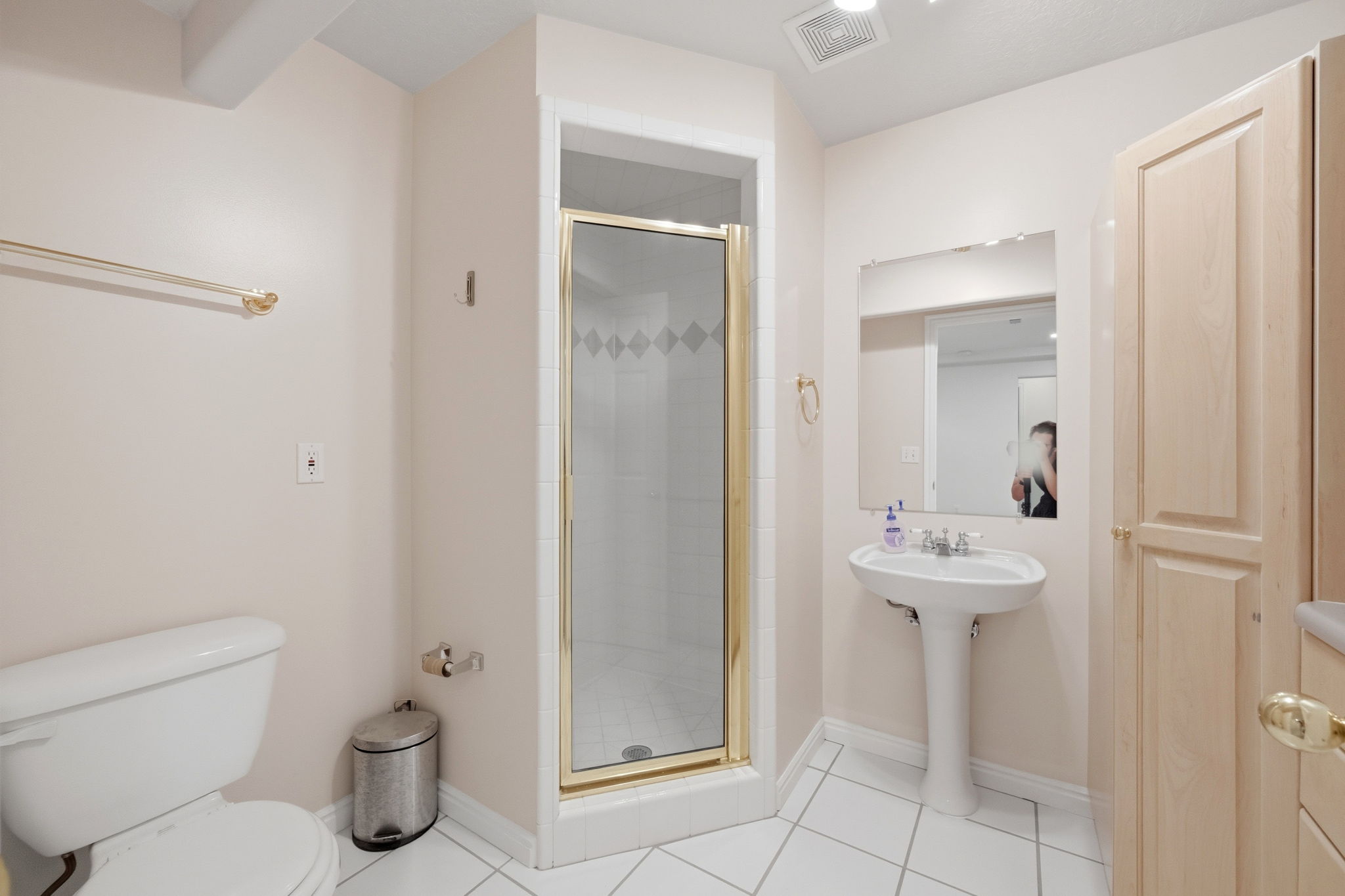 Bathroom featuring a glass-enclosed shower with gold-tone framing, a pedestal sink, and a mirrored vanity