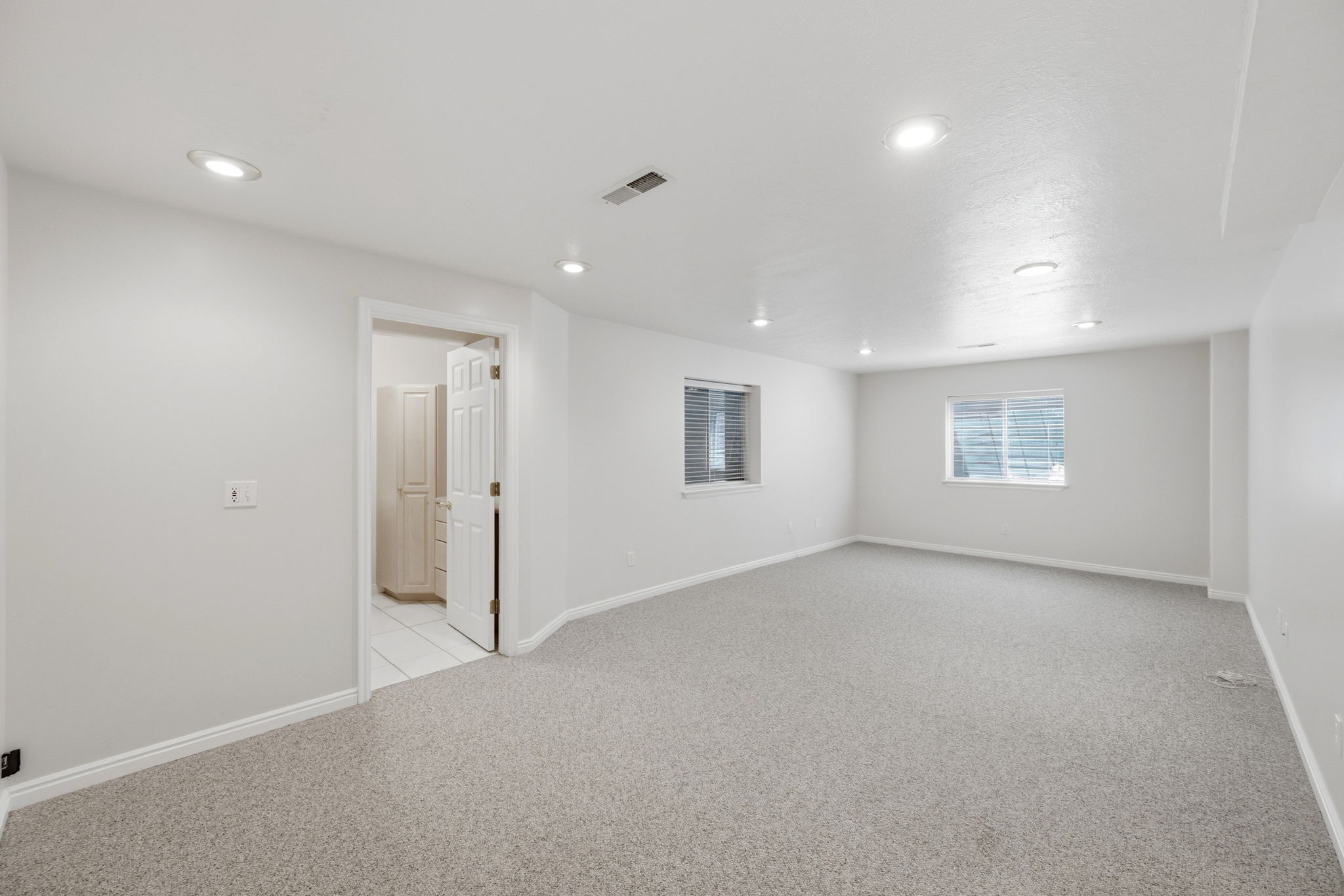 Spacious interior room featuring light gray carpeting, recessed lighting, and two windows with blinds