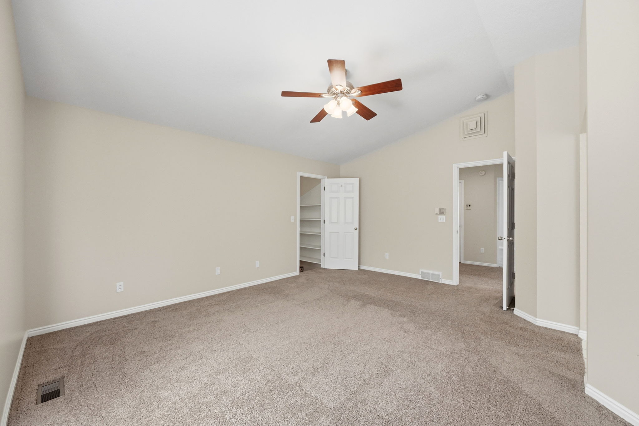 Spacious room featuring vaulted ceilings, neutral-toned carpeting, and a ceiling fan with integrated lighting