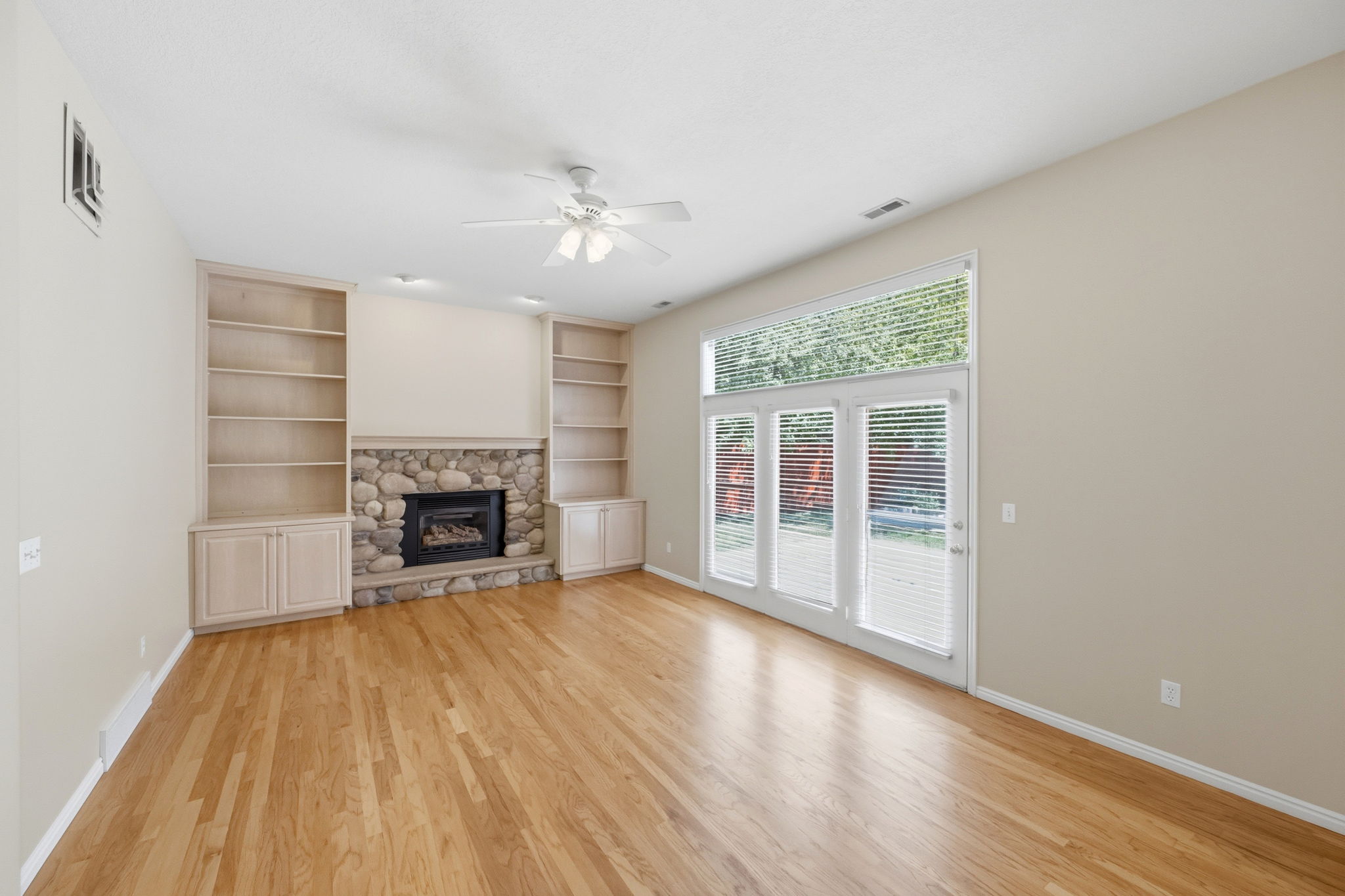 Hardwood flooring complements a stone-clad fireplace with gas insert, flanked by built-in bookshelves and cabinetry