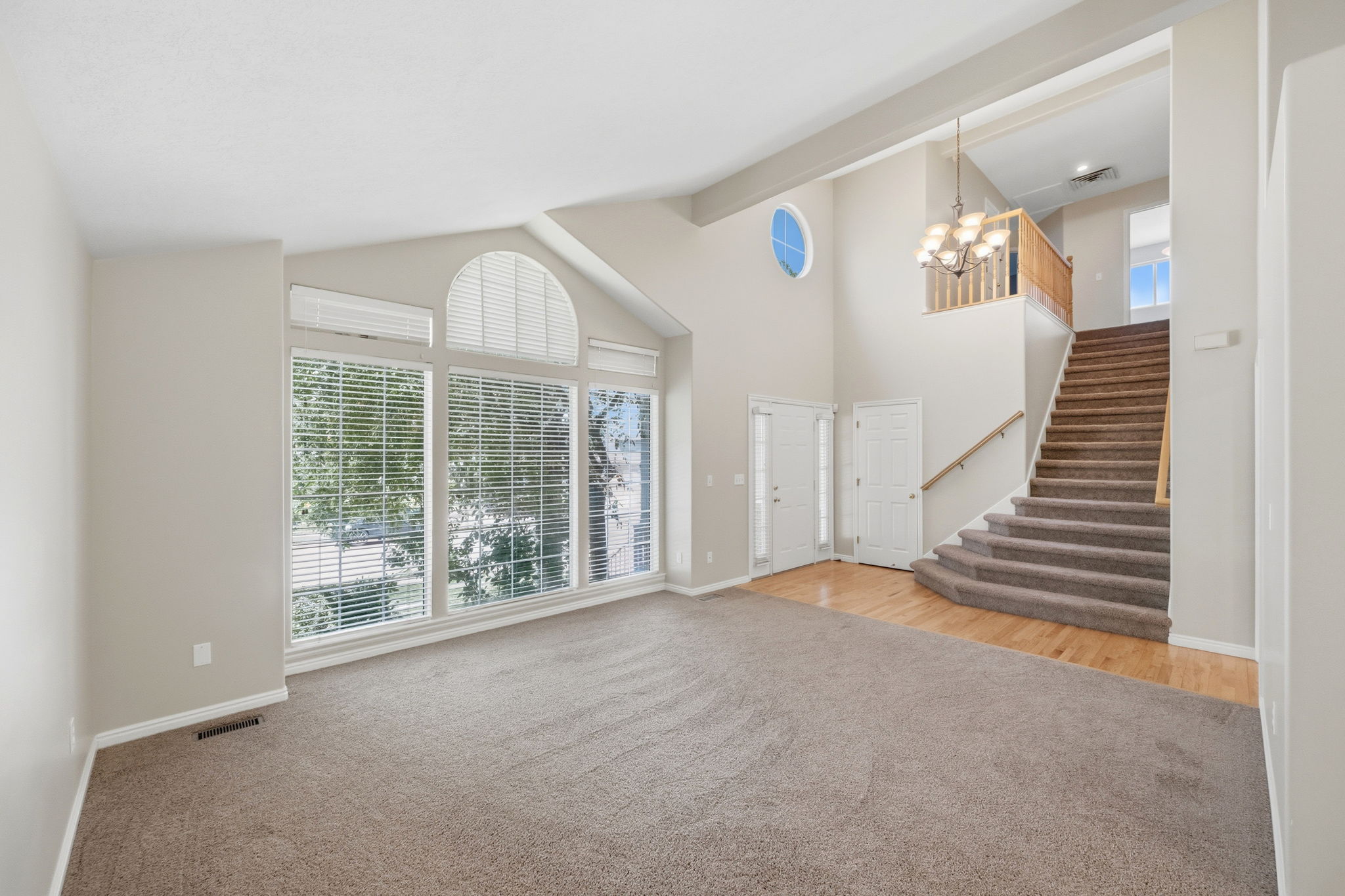 Vaulted great room featuring tall windows with arch detail, a grand staircase with wood railing, wood-finish flooring, and a round window