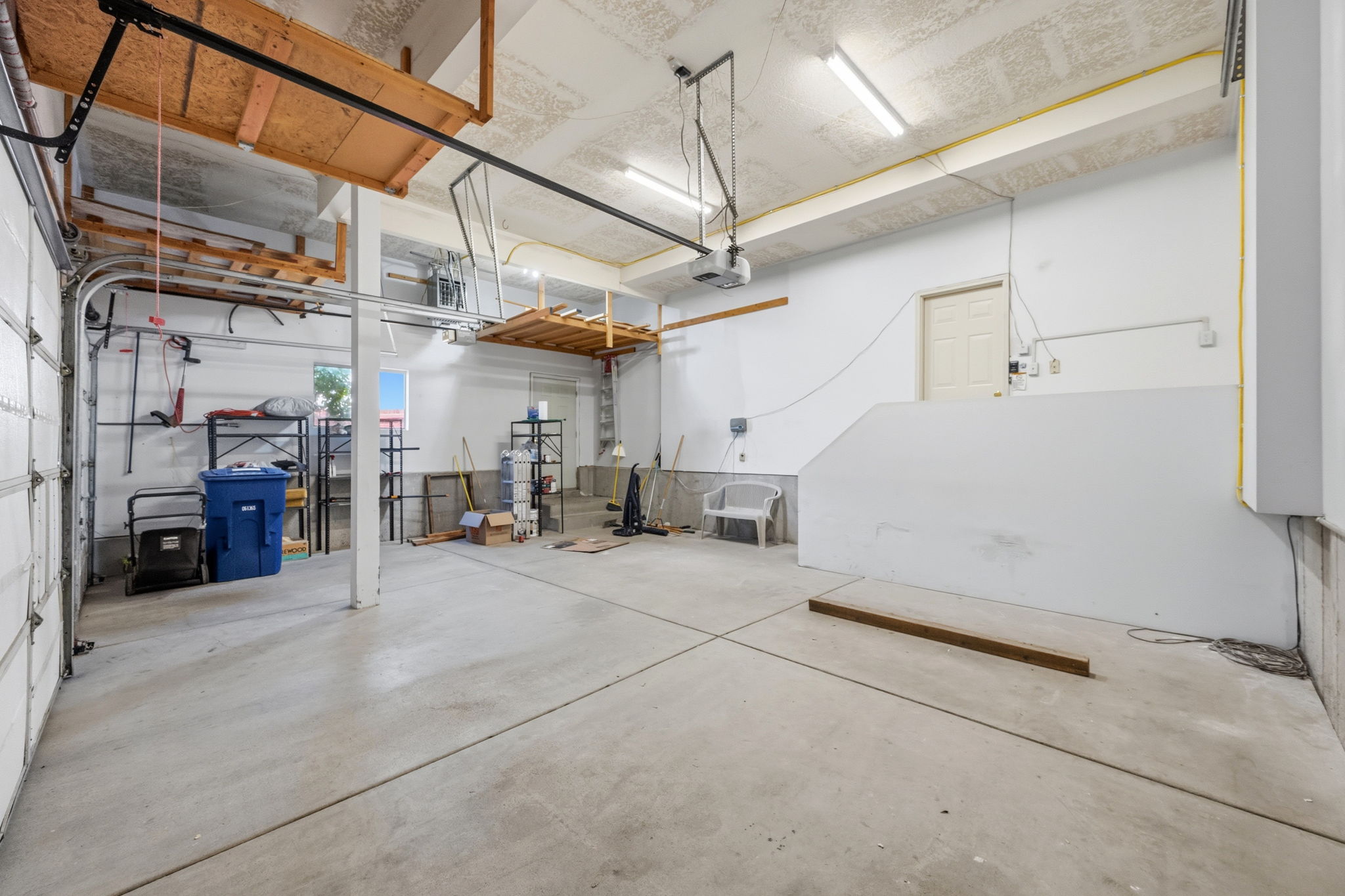 Spacious garage featuring a concrete floor, overhead storage shelving, fluorescent lighting, and a white access door