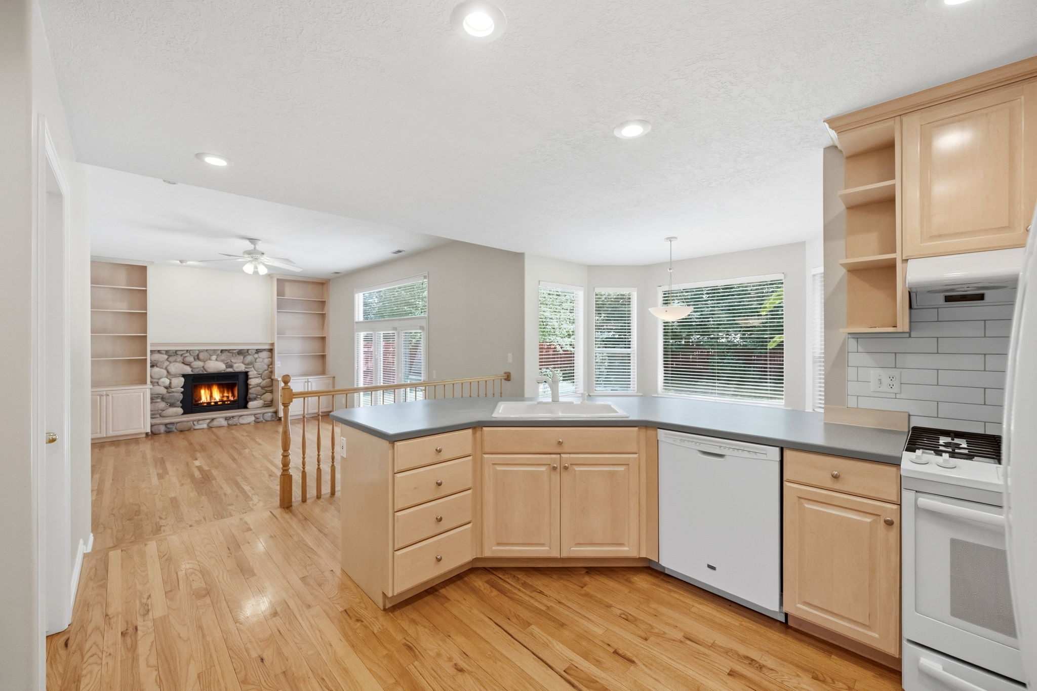 U-shaped kitchen with light wood cabinetry, gray countertops, and white appliances