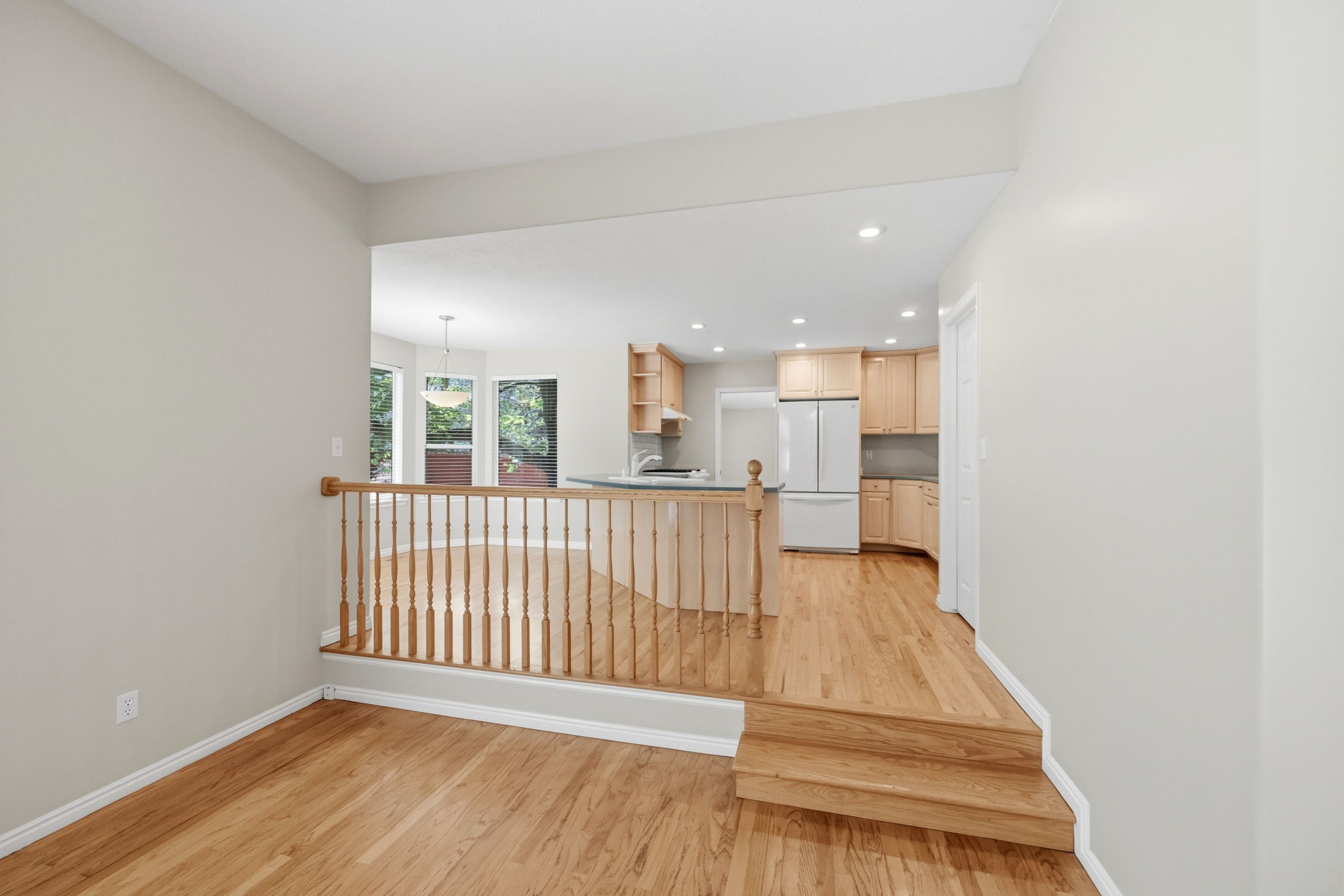 Split-level interior featuring warm wood-finish flooring, a wood banister, recessed lighting, and a kitchen with wood cabinetry and white appliances