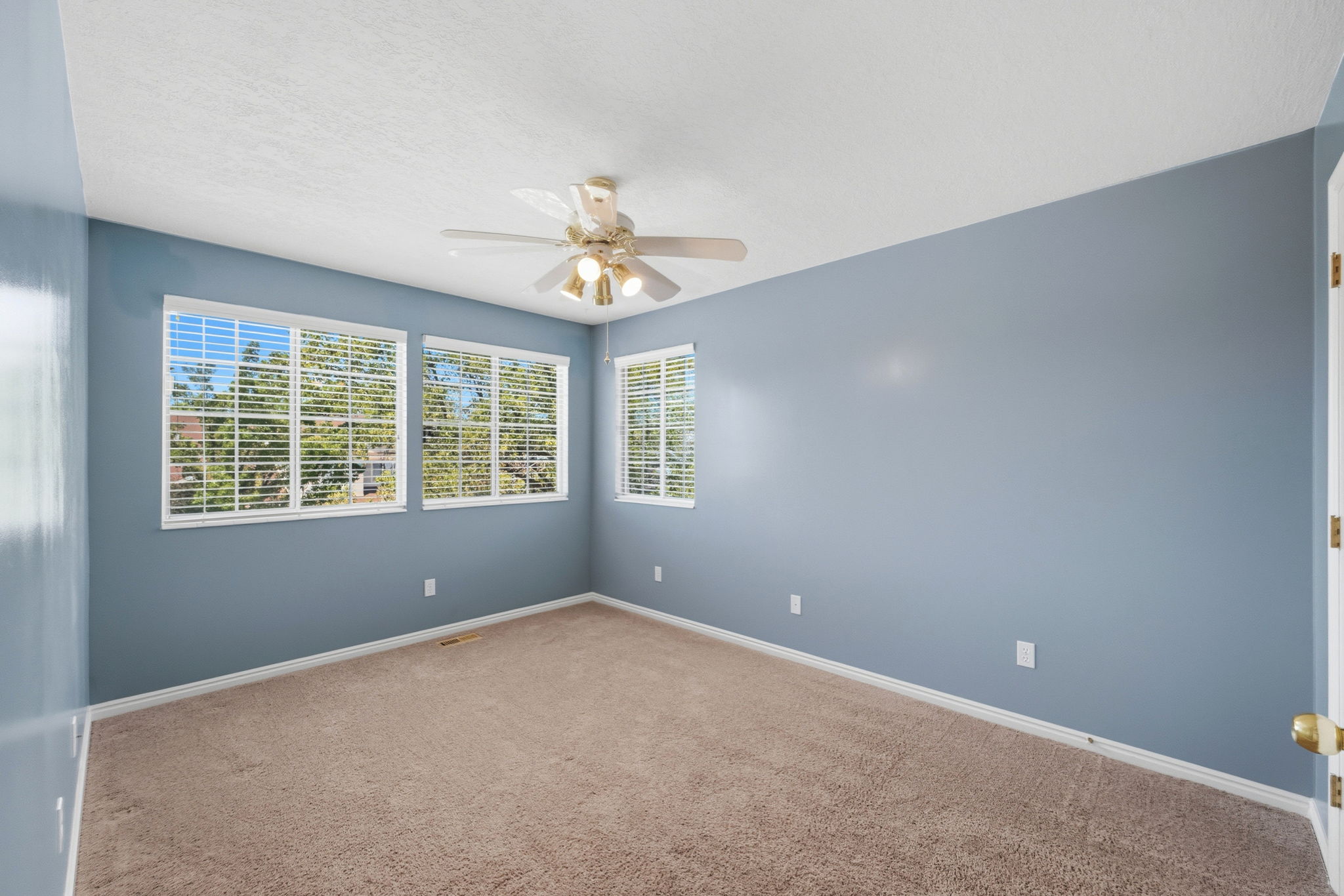 Room with light blue walls, multiple windows featuring white blinds, and a ceiling fan with integrated lighting