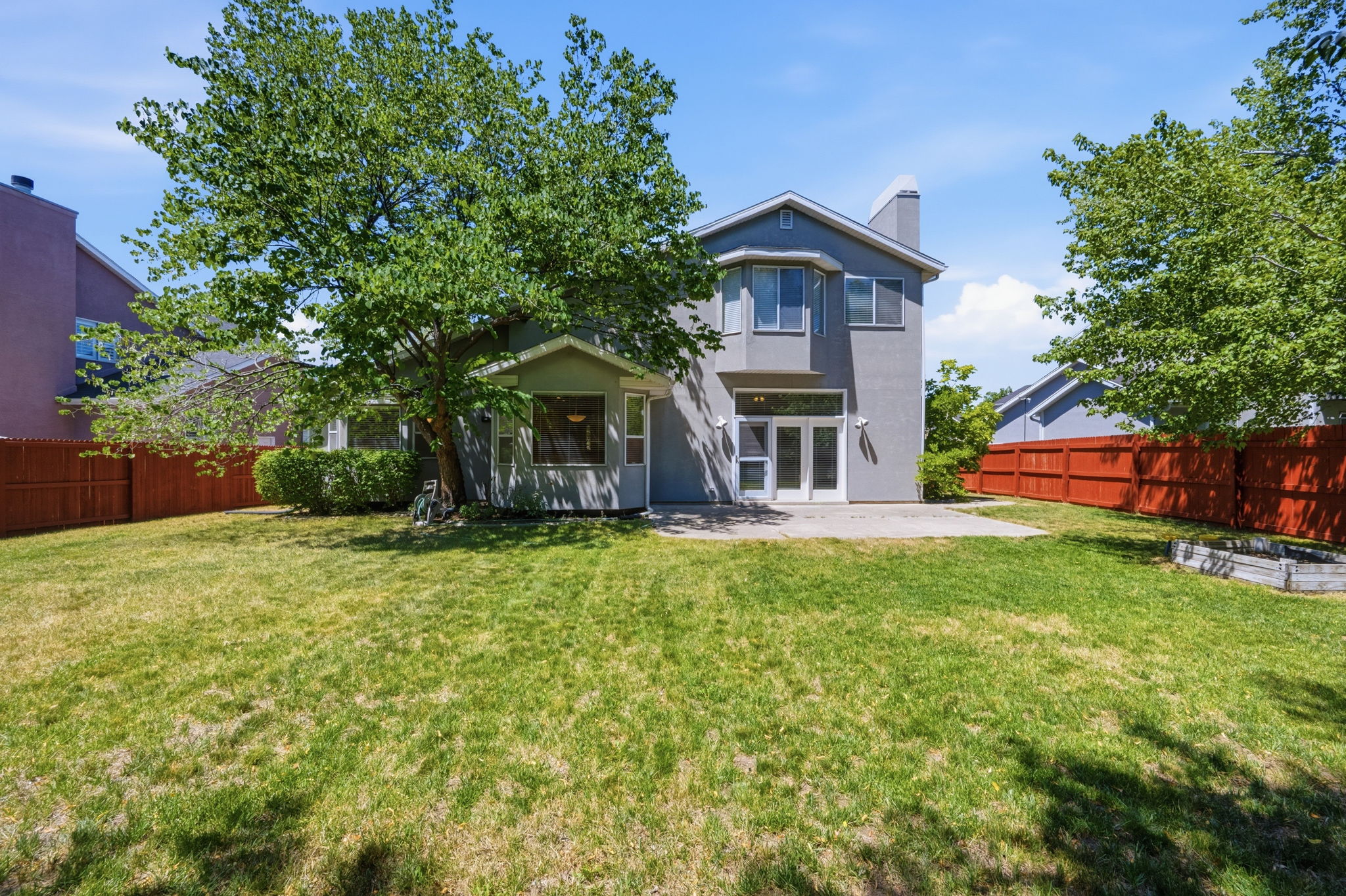 Expansive green lawn with mature trees and a solid wood perimeter fence